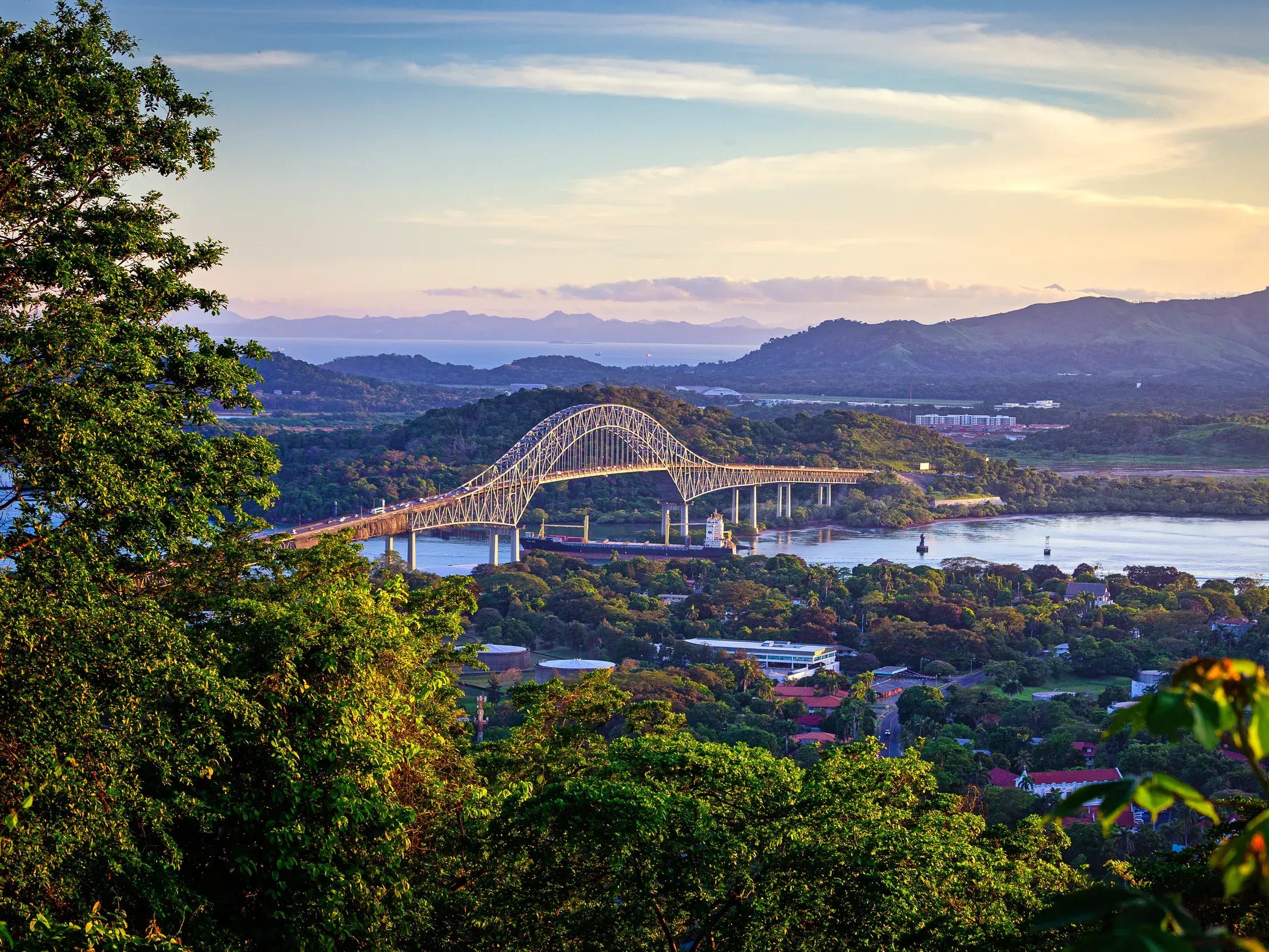 Panoramablick auf die Puente de las Américas über dem Panamakanal bei Sonnenuntergang, umgeben von tropischem Regenwald.