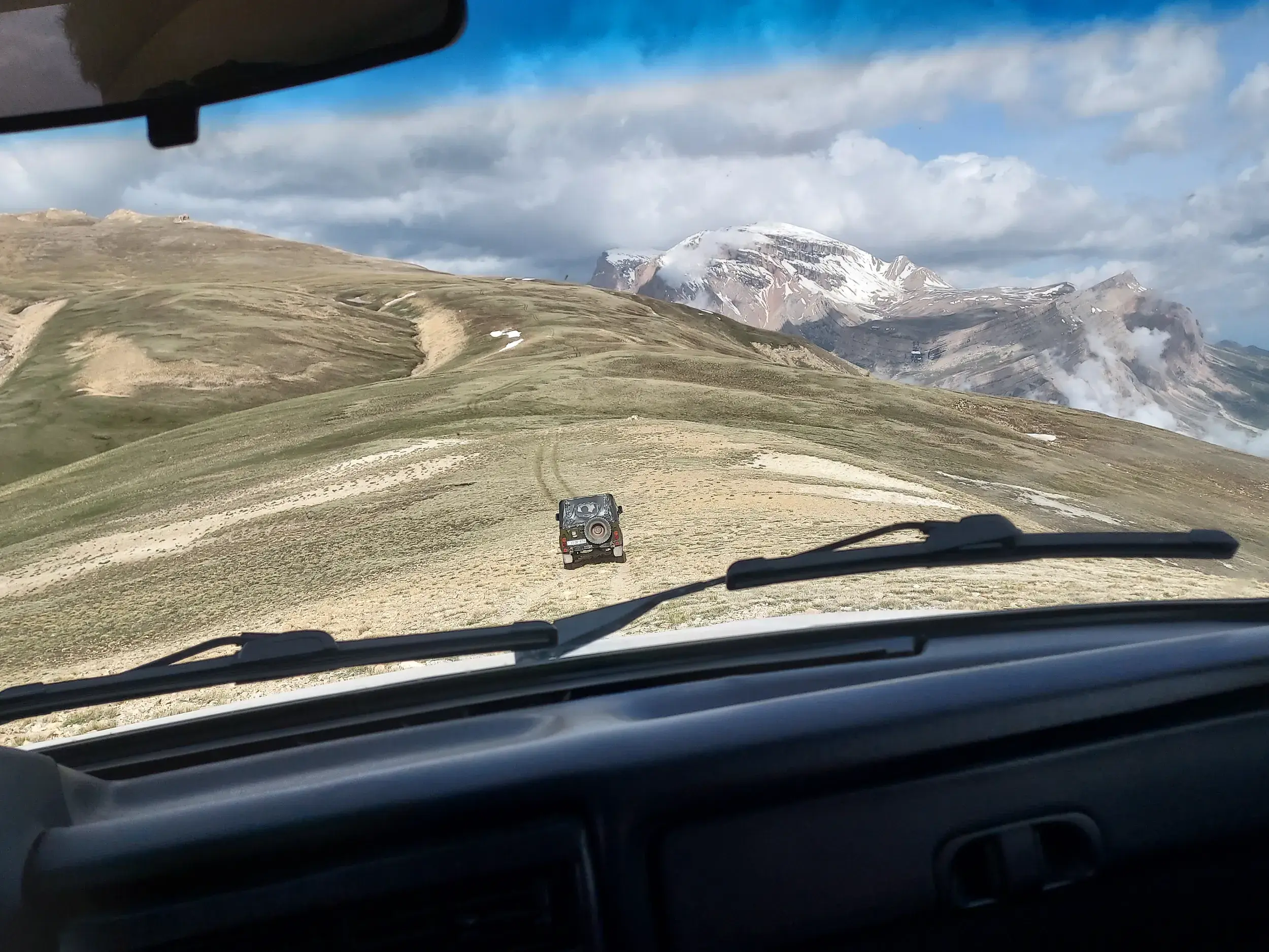 Fahrt mit einem Geländewagen durch die Hochebene des Großen Kaukasus, im Hintergrund der schneebedeckte Gipfel des Shahdag.