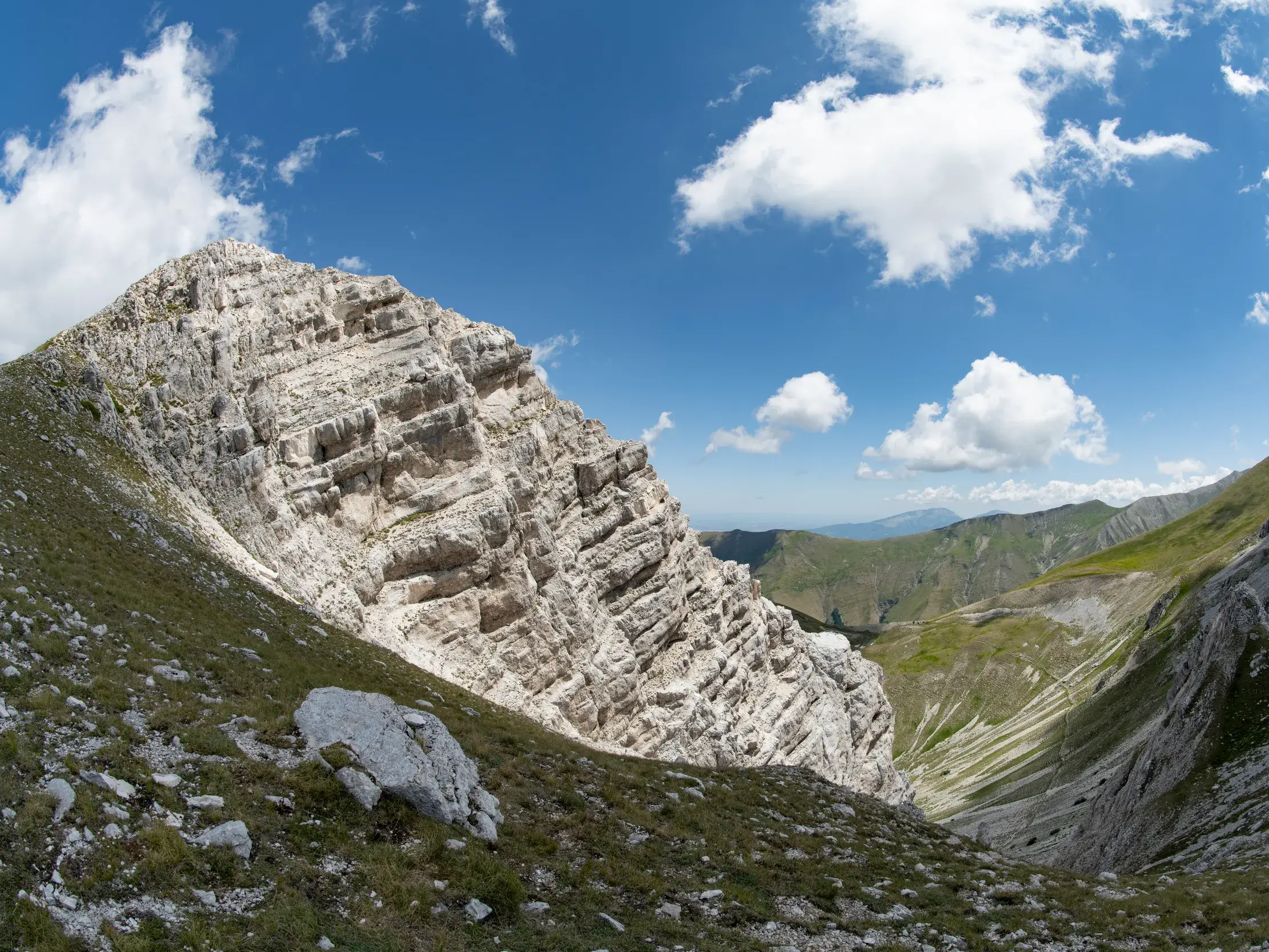 Felsiger Gipfel des Gran Sasso Massivs im Apennin, der sich über ein grünes, von Bergen umgebenes Tal erhebt.