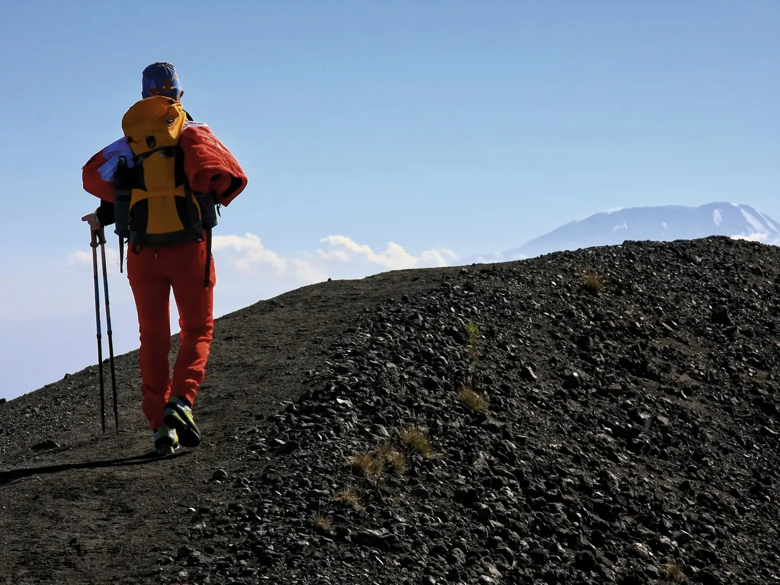 Wanderer in roter Kleidung beim Trekking auf dem steilen Vulkangrat des Mount Meru mit Blick auf den Kilimanjaro.