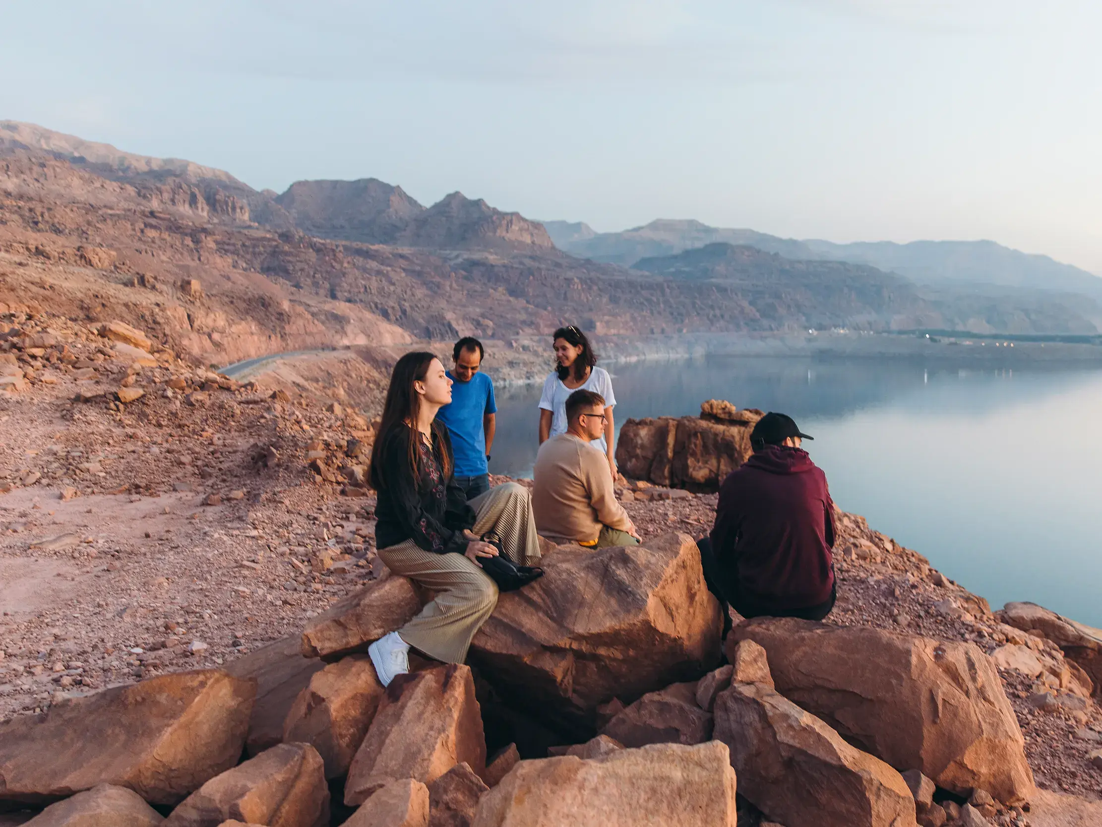 Eine junge Reisegruppe genießt bei Sonnenuntergang den Panoramablick von einem Felsen über das Tote Meer in Jordanien.