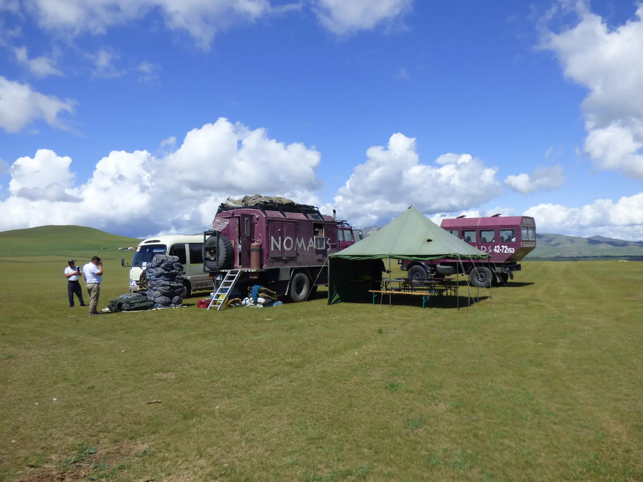 Mobiles Camp mit Expeditionsfahrzeugen und aufgestelltem Zelt in der weiten, grünen Steppenlandschaft der Mongolei.