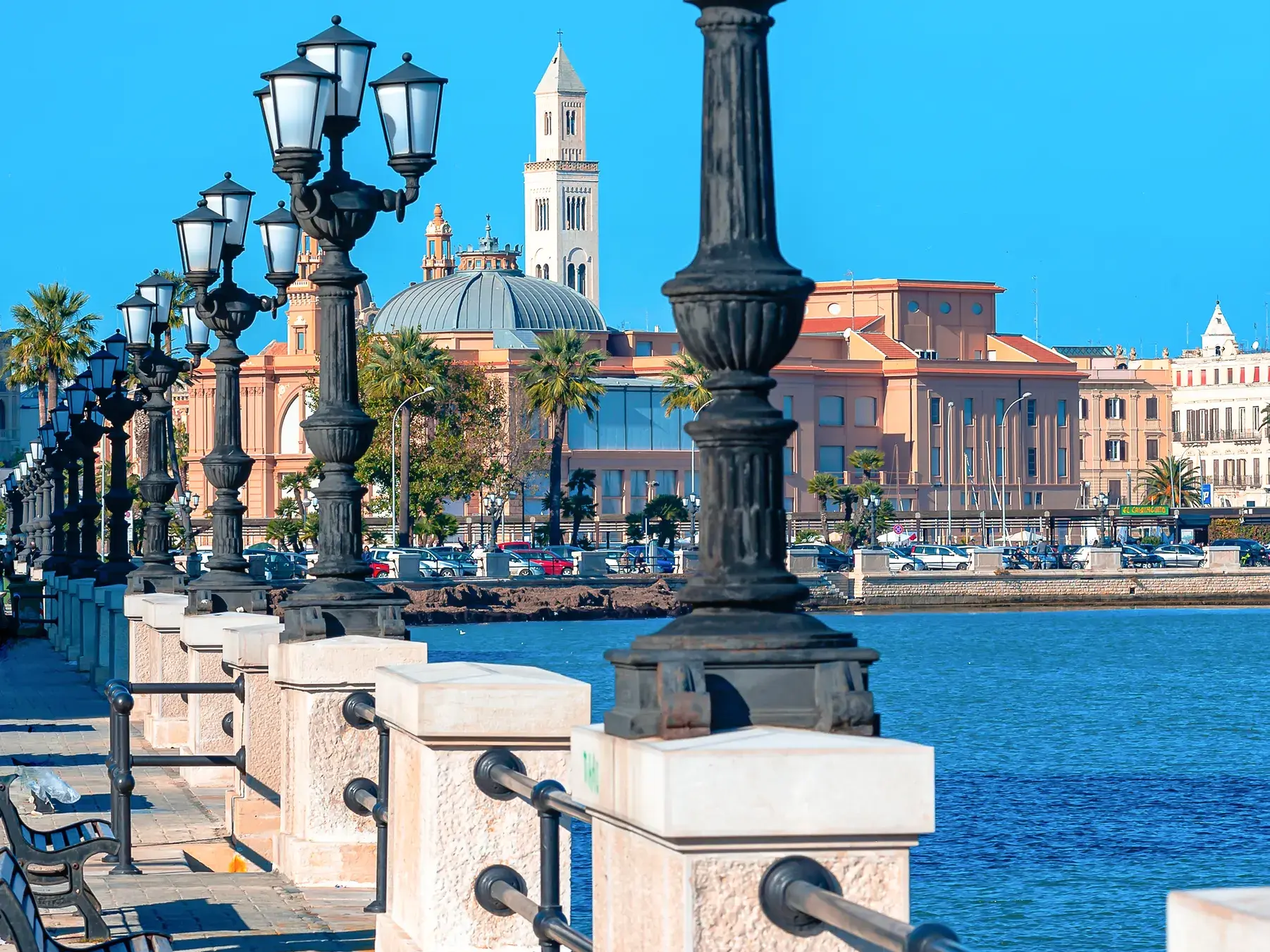 Schwarze Laternen säumen die Uferpromenade in Bari mit Blick auf die sonnige Skyline der apulischen Hauptstadt am Meer.