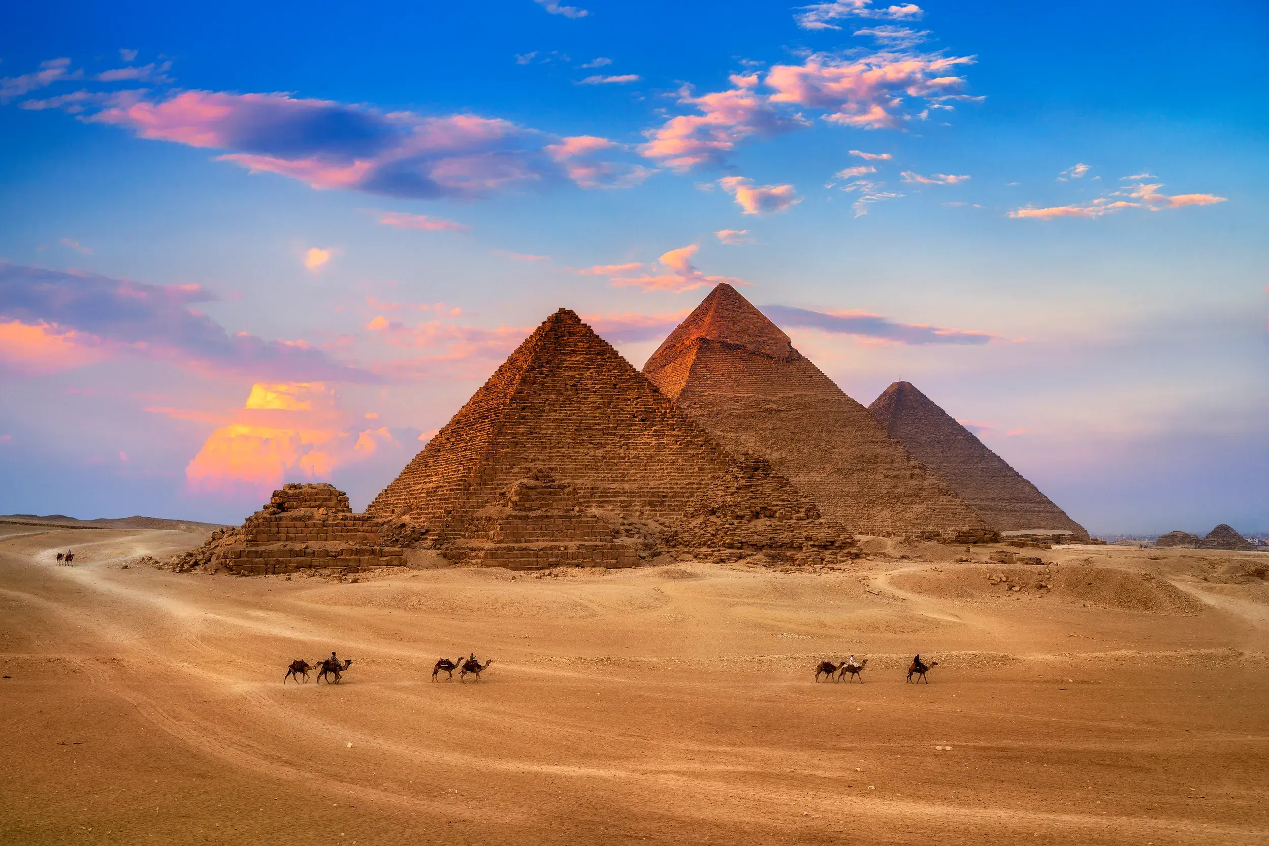 Die Pyramiden von Gizeh in Ägypten mit Kamelreitern im Wüstensand bei Sonnenuntergang.