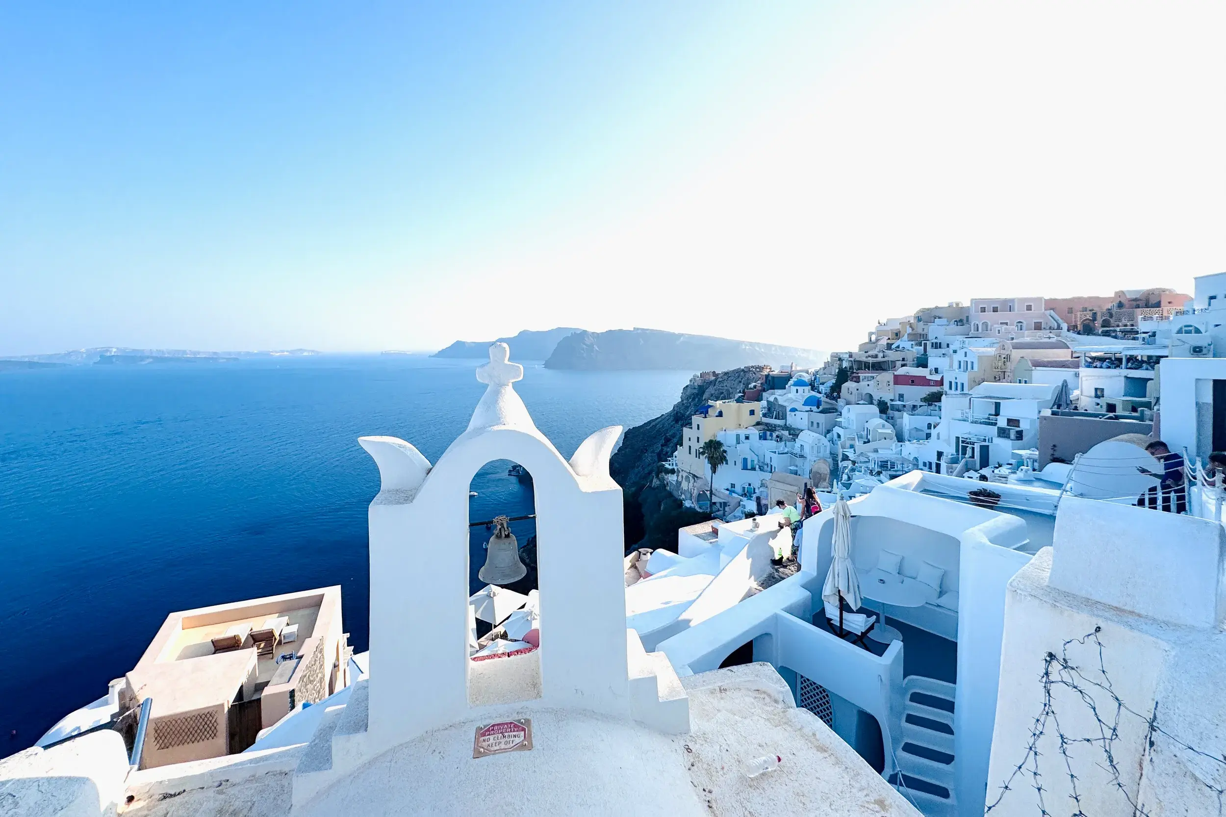 Weißer Glockenturm auf Santorin mit Blick über die Stadt Fira, die sich an die Klippen der Caldera über der blauen Ägäis schmiegt.