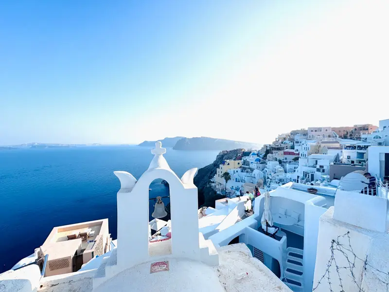Weißer Glockenturm auf Santorin mit Blick über die Stadt Fira, die sich an die Klippen der Caldera über der blauen Ägäis schmiegt.