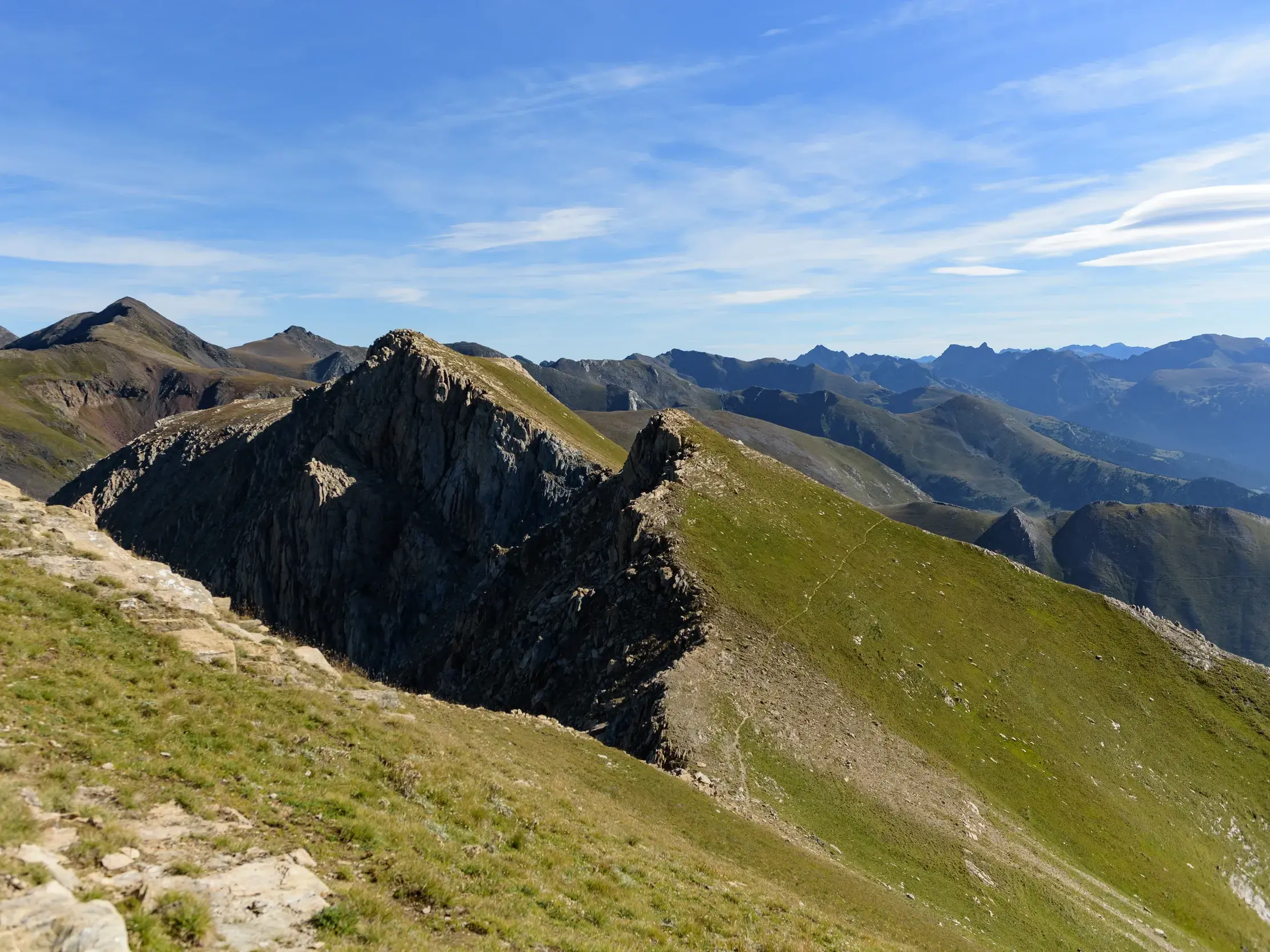 Wanderweg entlang eines schmalen Berggrats zum Gipfel des Pic de la Serrera in den andorranischen Pyrenäen unter blauem Himmel.