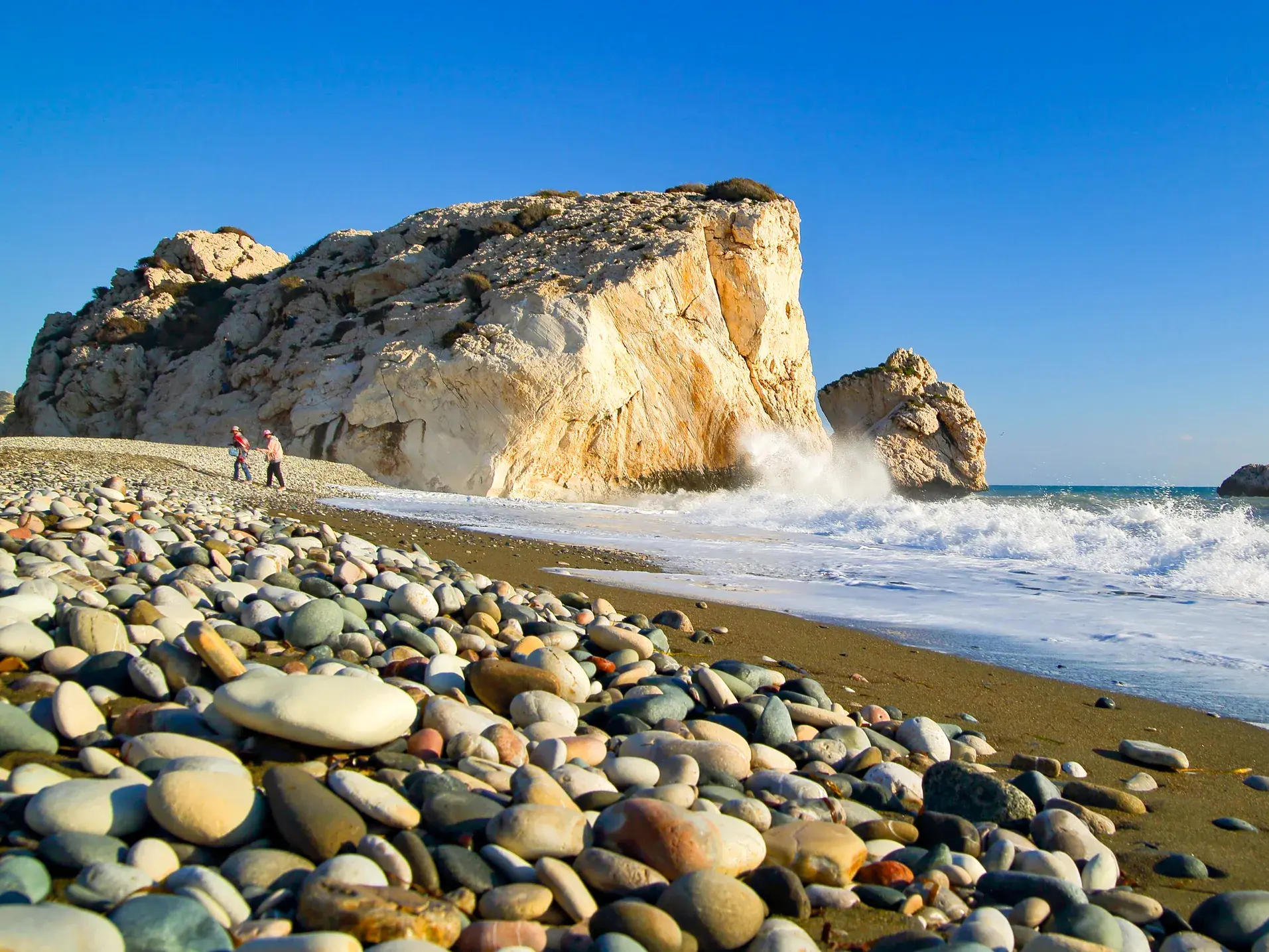 Zwei Wanderer am Kieselstrand am sagenumwobenen Felsen der Aphrodite, Petra tou Romiou, wo Wellen an die Küste Zyperns schlagen.