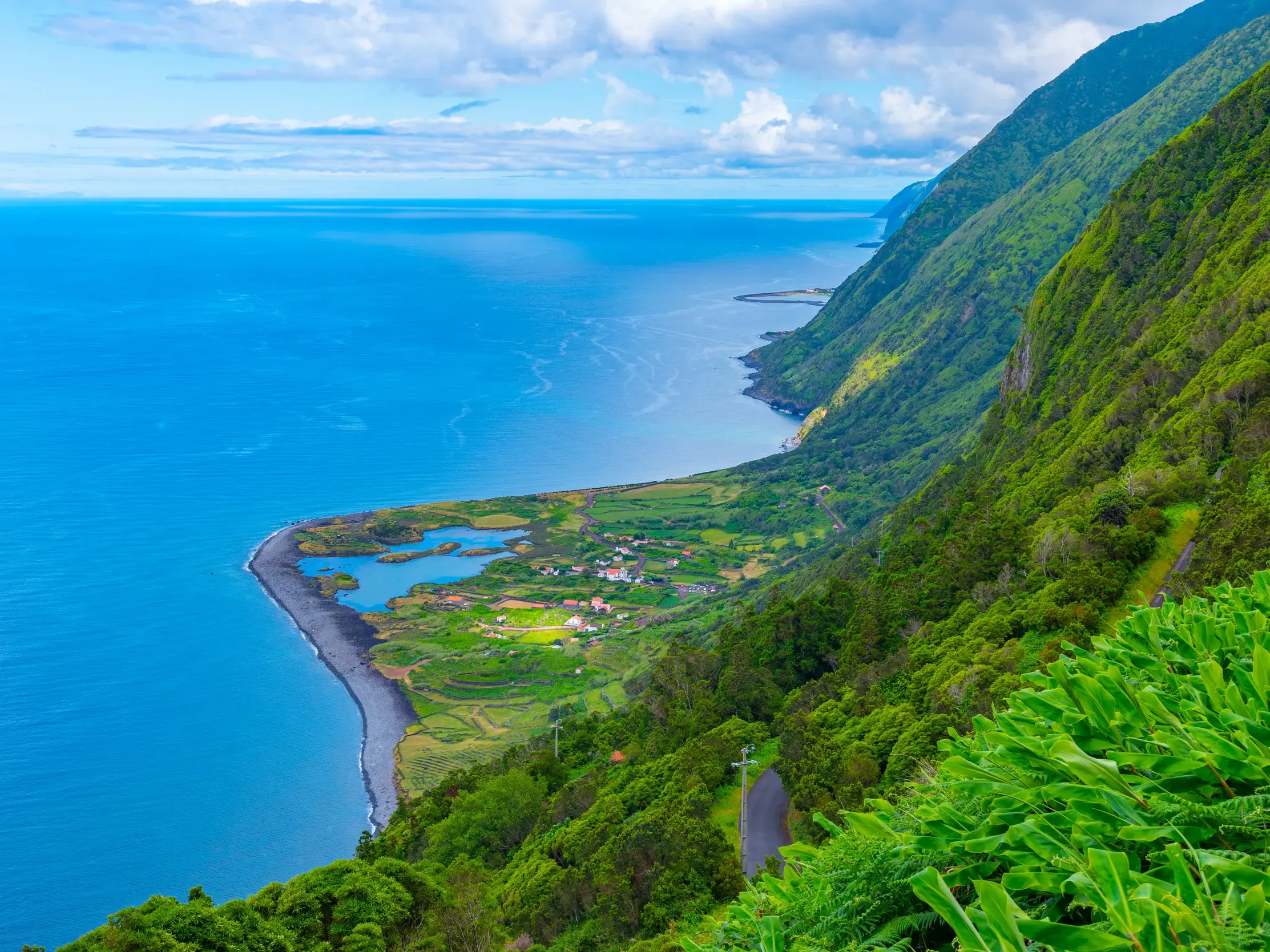 Aussicht von der Steilküste auf Sao Jorge auf die grün bewachsene Lavazunge (Faja) mit Seen und dunklem Strand am Atlantik.