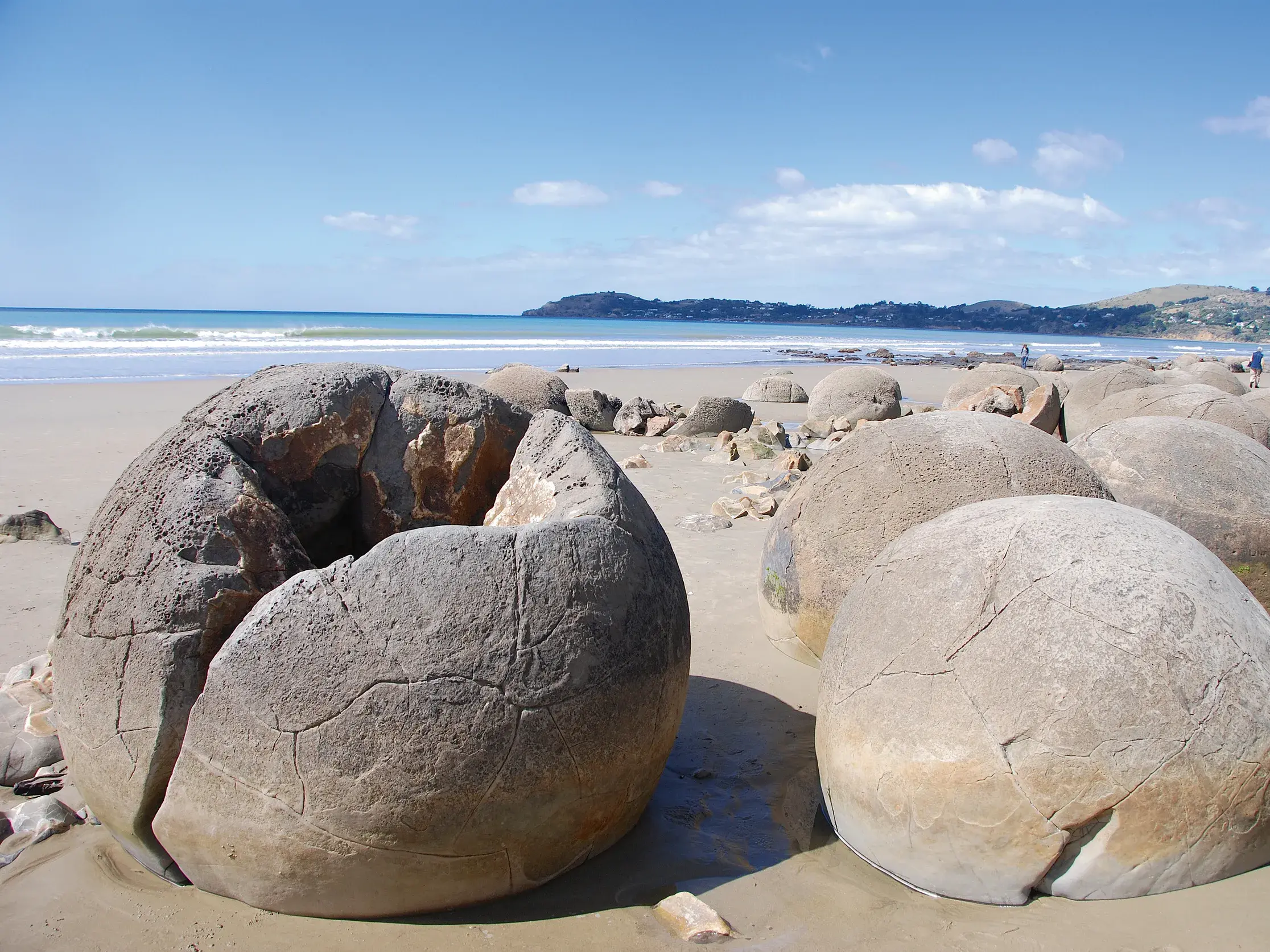 Die einzigartigen, kugelförmigen Moeraki Boulders an der Küste Neuseelands, verstreut auf dem Sandstrand am Meer.
