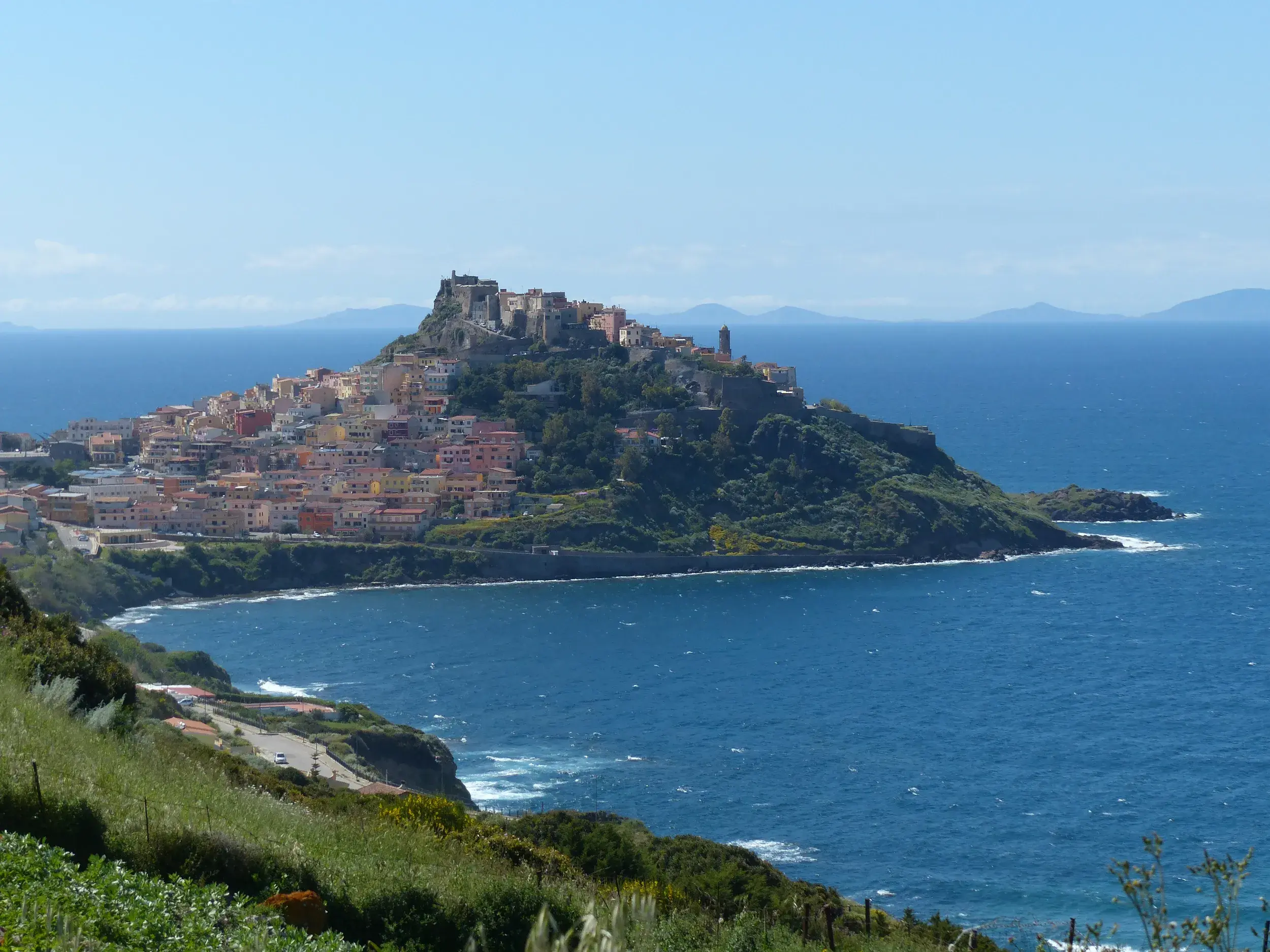 Weitblick von einem Wanderweg auf das Burgdorf Castelsardo, das majestätisch auf einem Felsen über dem blauen Meer thront.