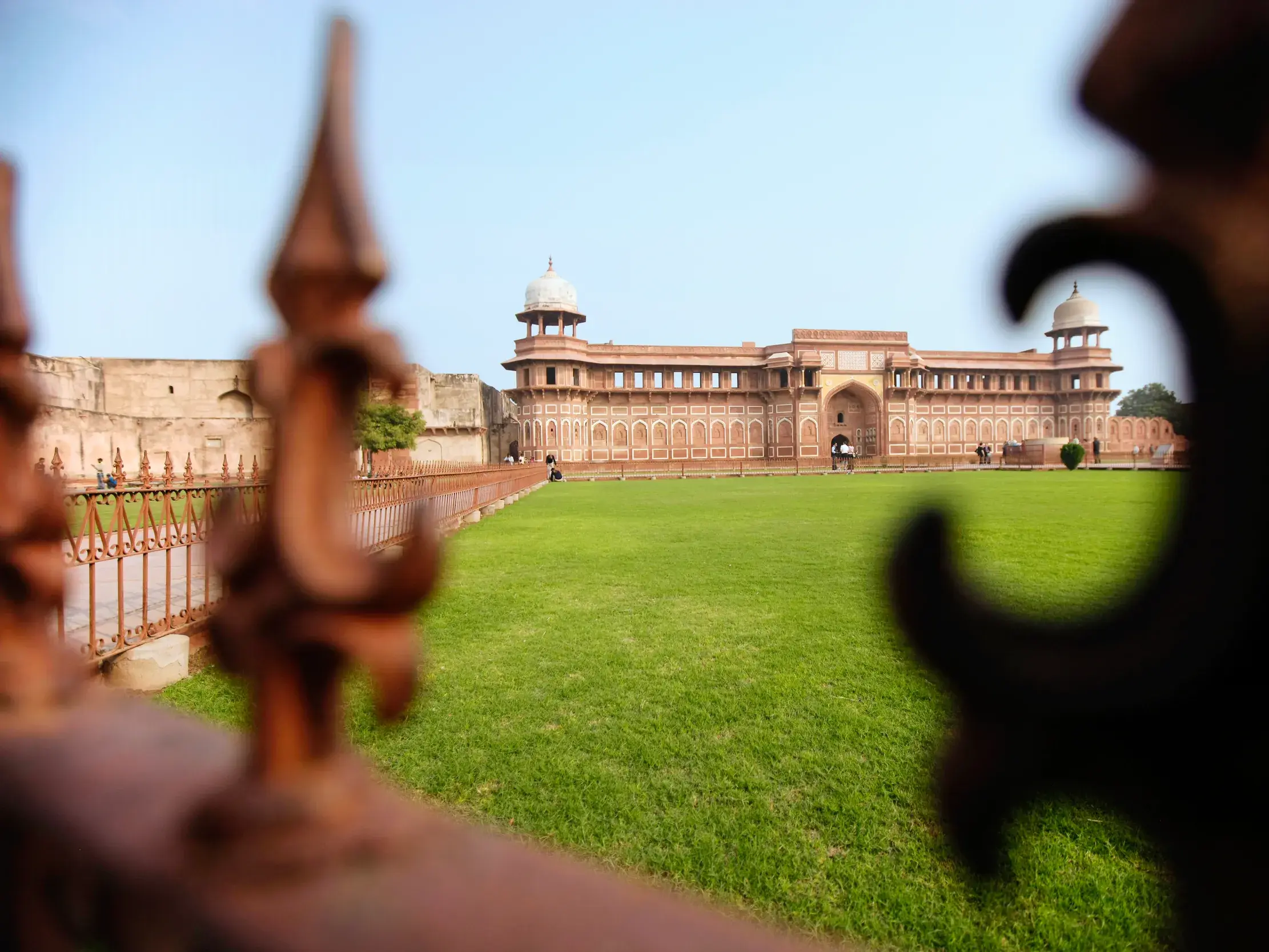 Gerahmter Blick auf den Jahangiri Palast im Roten Fort in Agra. Die rote Sandsteinfestung der Mogulkaiser erhebt sich hinter einem grünen Rasen.