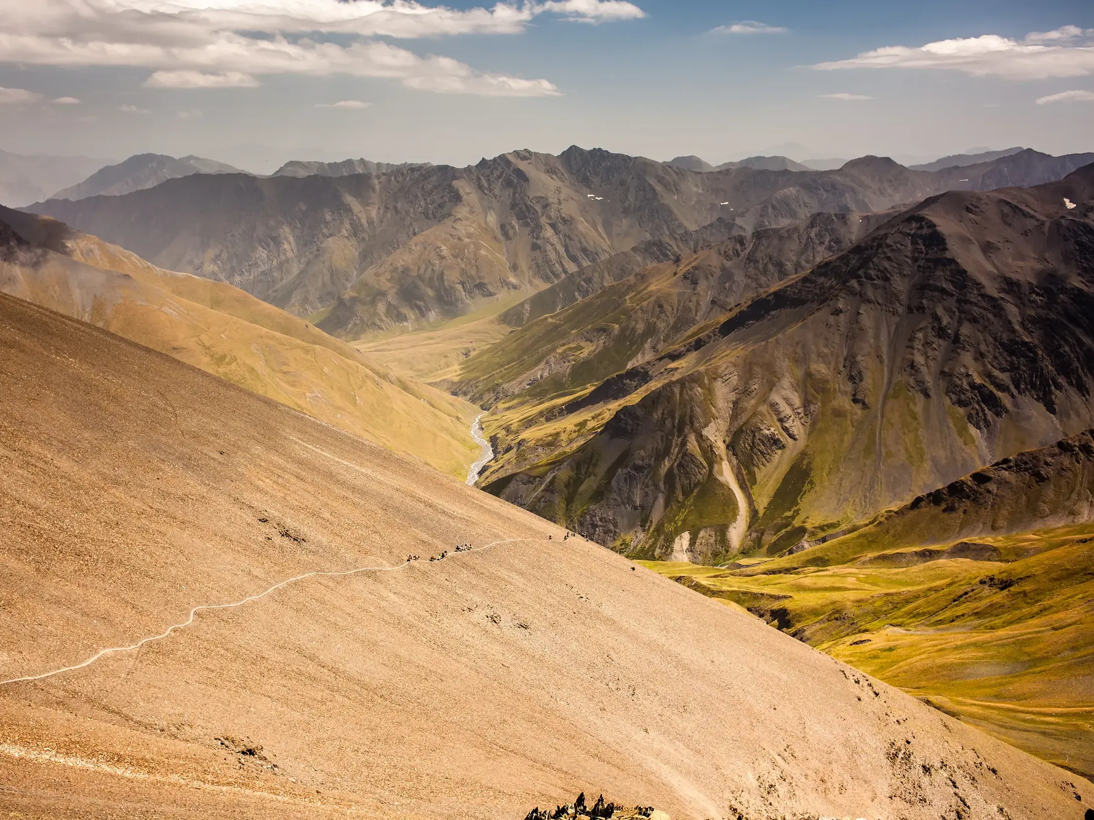 Eine Trekking-Gruppe wandert auf einem schmalen Pfad über eine steile Geröllhalde zum Atsunta-Pass im georgischen Kaukasus.