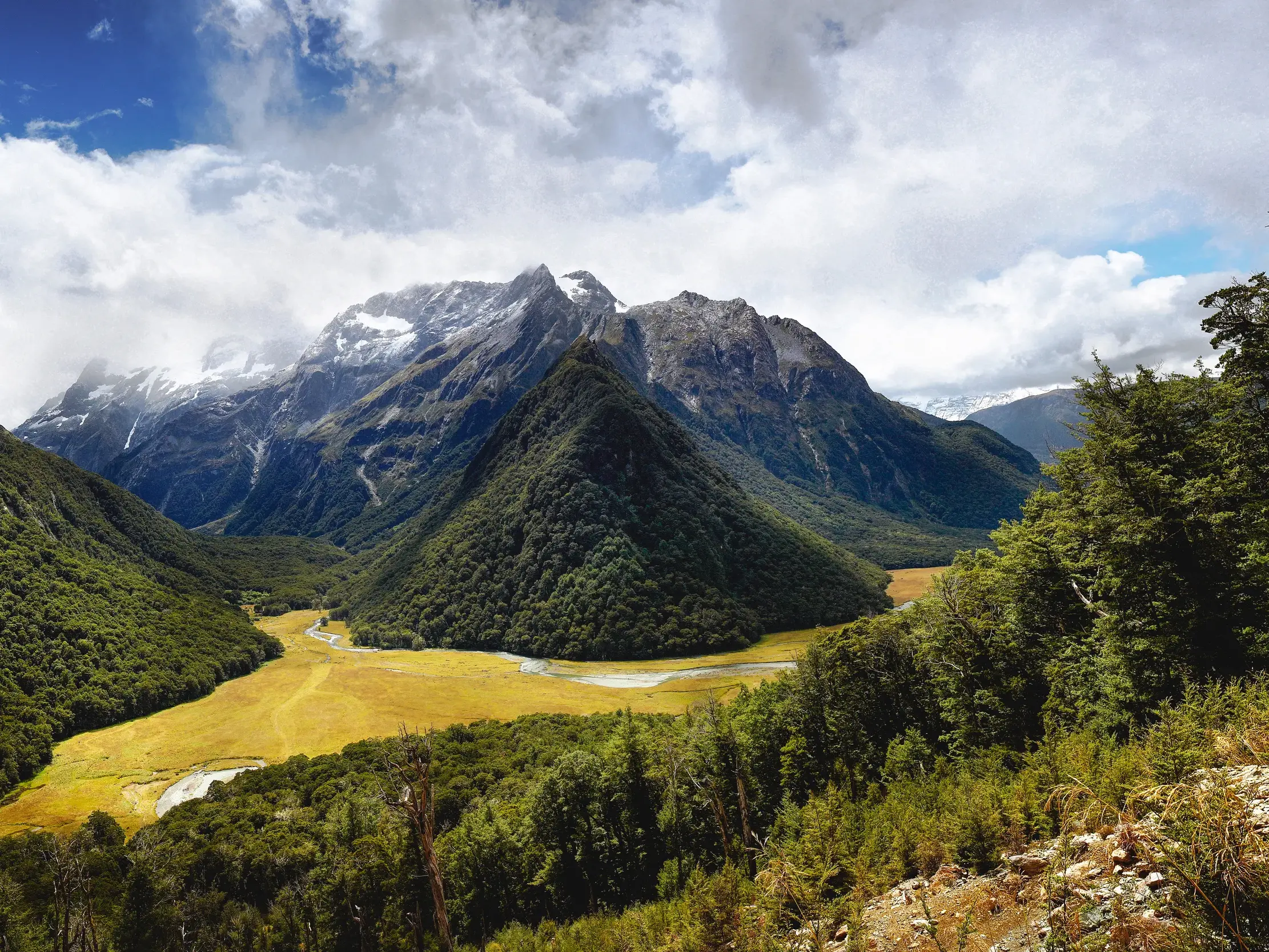 Aussicht vom Wanderweg des Routeburn Track in ein weites, sonniges Tal mit schneebedeckten Bergen im Fjordland Nationalpark.