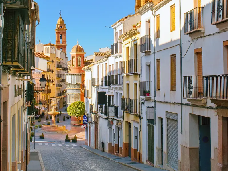Sonnige Gasse mit weißen Fassaden und Blick auf den Kirchturm in Antequera