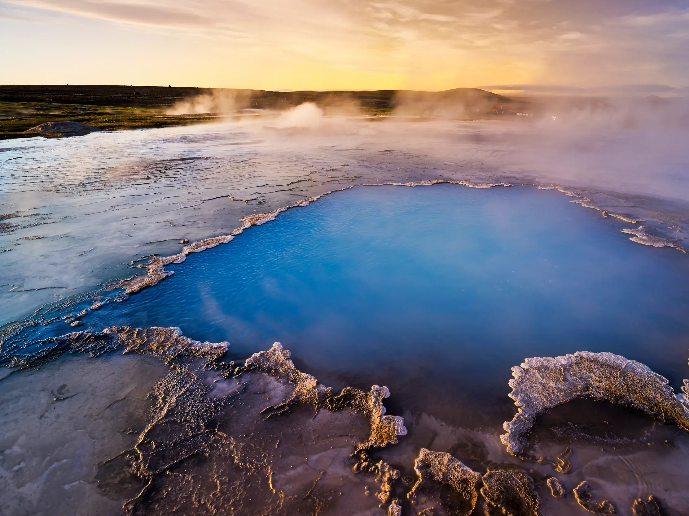 Eine leuchtend blaue heiße Quelle dampft in der archaischen Landschaft des Geothermalgebiets Hveravellir im Hochland von Island.