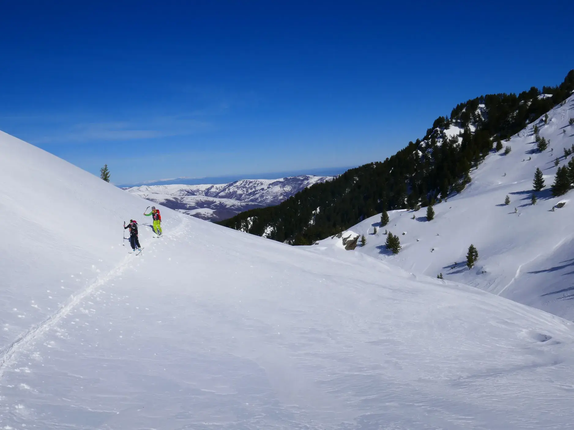 Zwei Skitourengeher auf dem Aufstieg durch unberührten Tiefschnee an einem sonnigen Hang im Sharr-Gebirge im Kosovo.