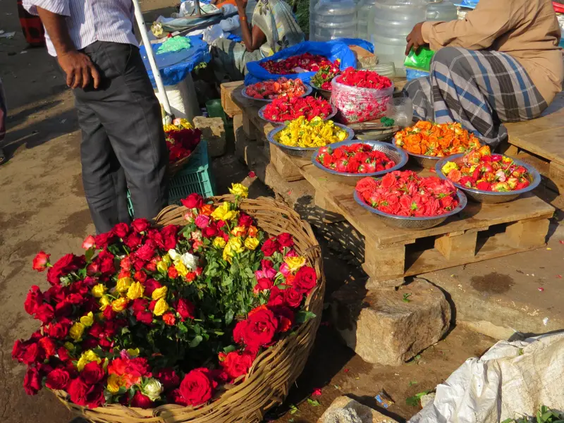 Farbenprächtige Rosen und Blütenblätter in Schalen auf einem belebten Blumenmarkt in Madurai, Südindien.