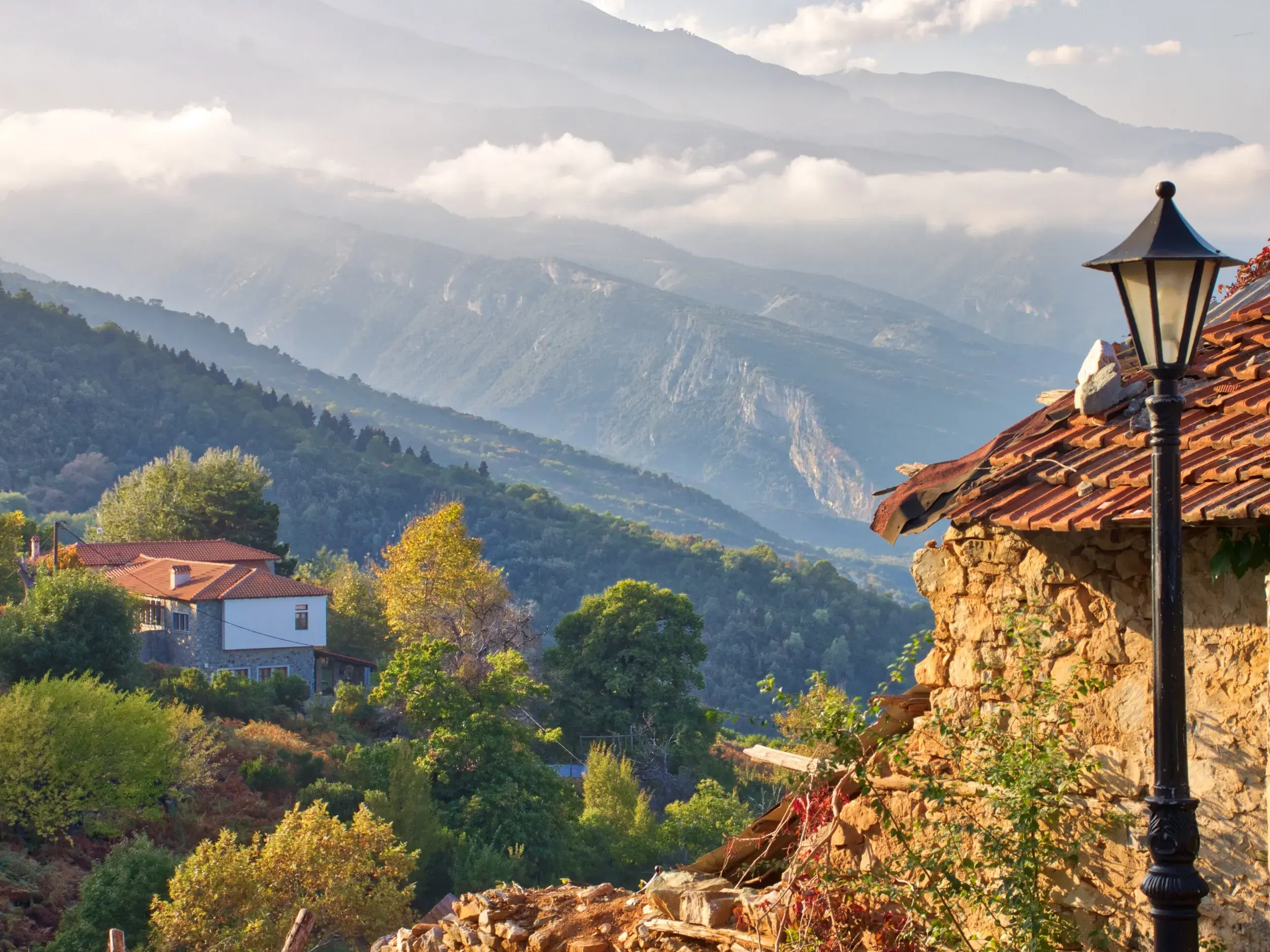 Malerischer Ausblick vom Bergdorf Palaios Panteleimonas über grüne Hänge auf das wolkenverhangene Olymp-Massiv in Griechenland.