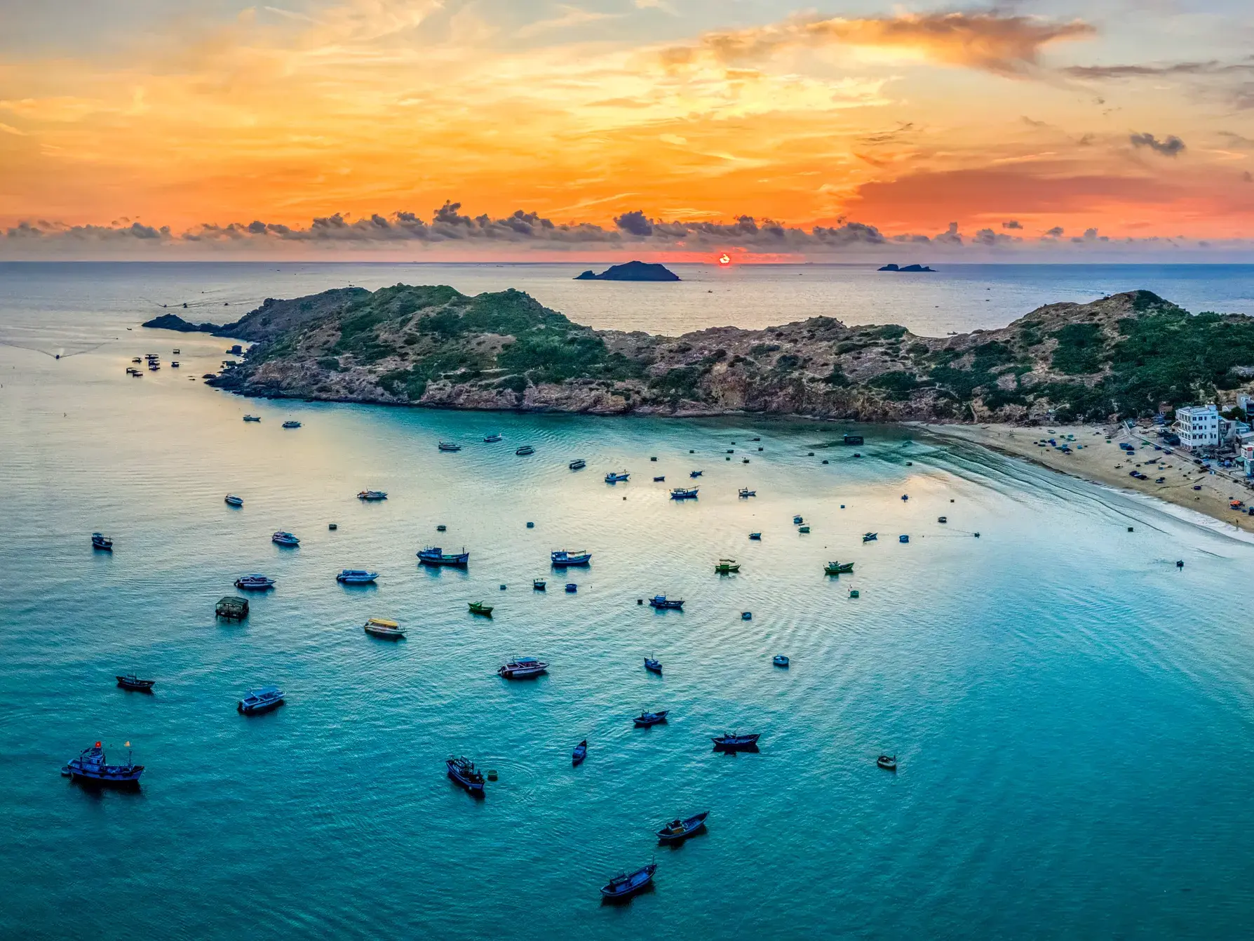 Zahlreiche Fischerboote ankern im türkisen Wasser der malerischen Bucht von Quy Nhon während des leuchtenden Sonnenuntergangs.
