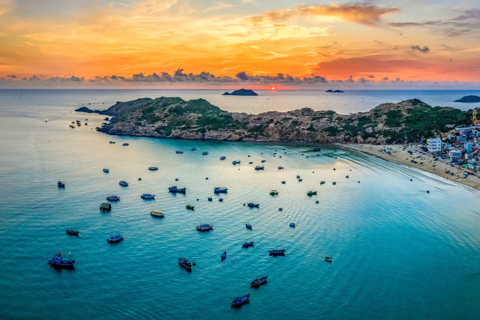 Zahlreiche Fischerboote ankern im türkisen Wasser der malerischen Bucht von Quy Nhon während des leuchtenden Sonnenuntergangs.