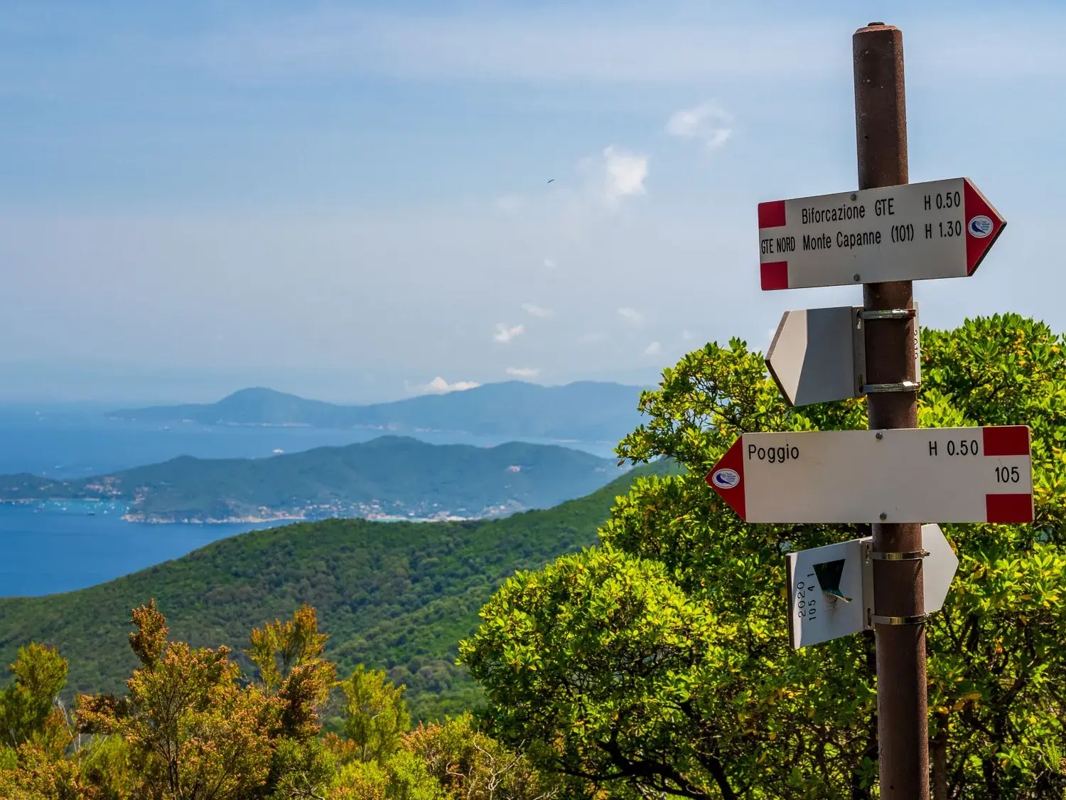 Wegweiser am GTE-Wanderweg nach Poggio mit Panoramablick über die bewaldete Küste Elbas und das tiefblaue Mittelmeer.