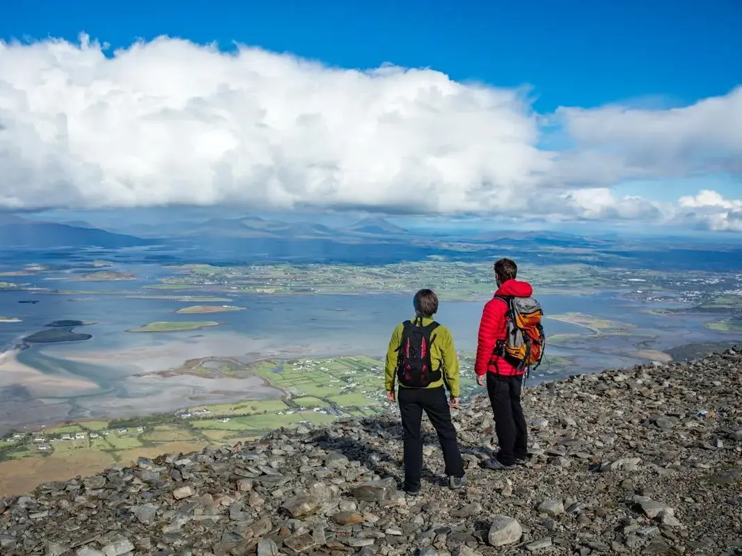 Zwei Wanderer genießen vom felsigen Gipfel des Croagh Patrick die weite Aussicht auf die Inseln der Clew Bay in Irland.