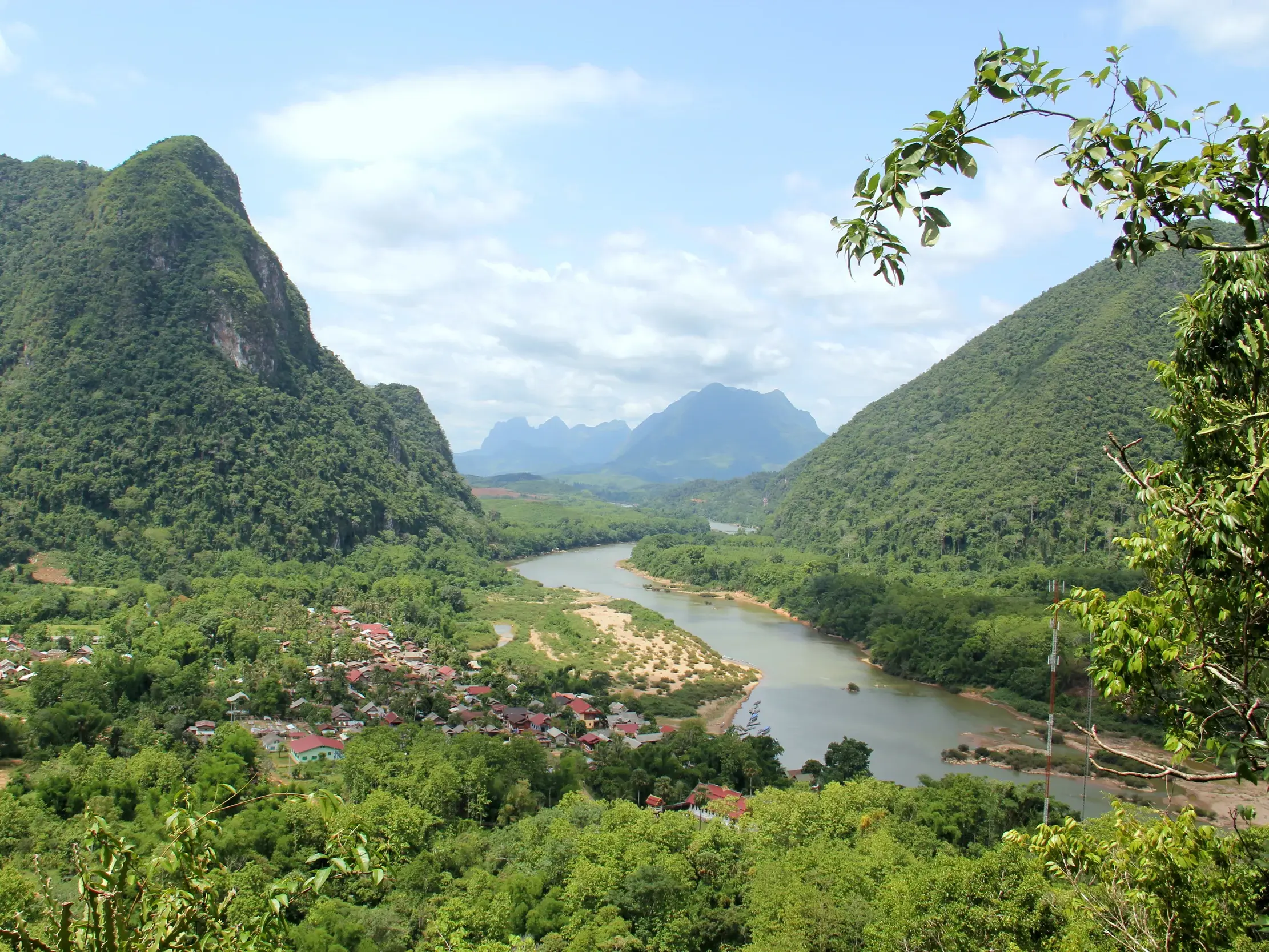Panoramablick von einem Aussichtspunkt auf den Nam Ou Fluss, der sich durch grüne Karstberge und ein Dorf in Nordlaos schlängelt.