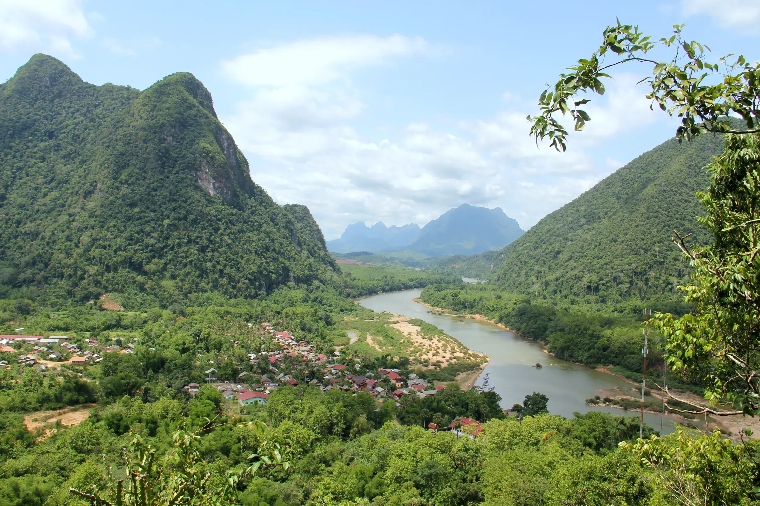 Panoramablick von einem Aussichtspunkt auf den Nam Ou Fluss, der sich durch grüne Karstberge und ein Dorf in Nordlaos schlängelt.