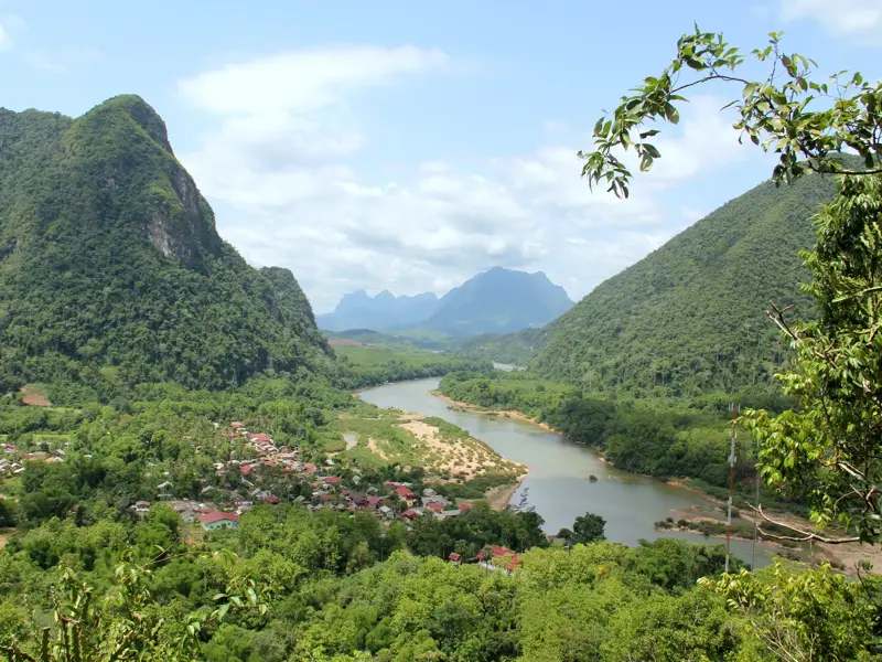 Panoramablick von einem Aussichtspunkt auf den Nam Ou Fluss, der sich durch grüne Karstberge und ein Dorf in Nordlaos schlängelt.