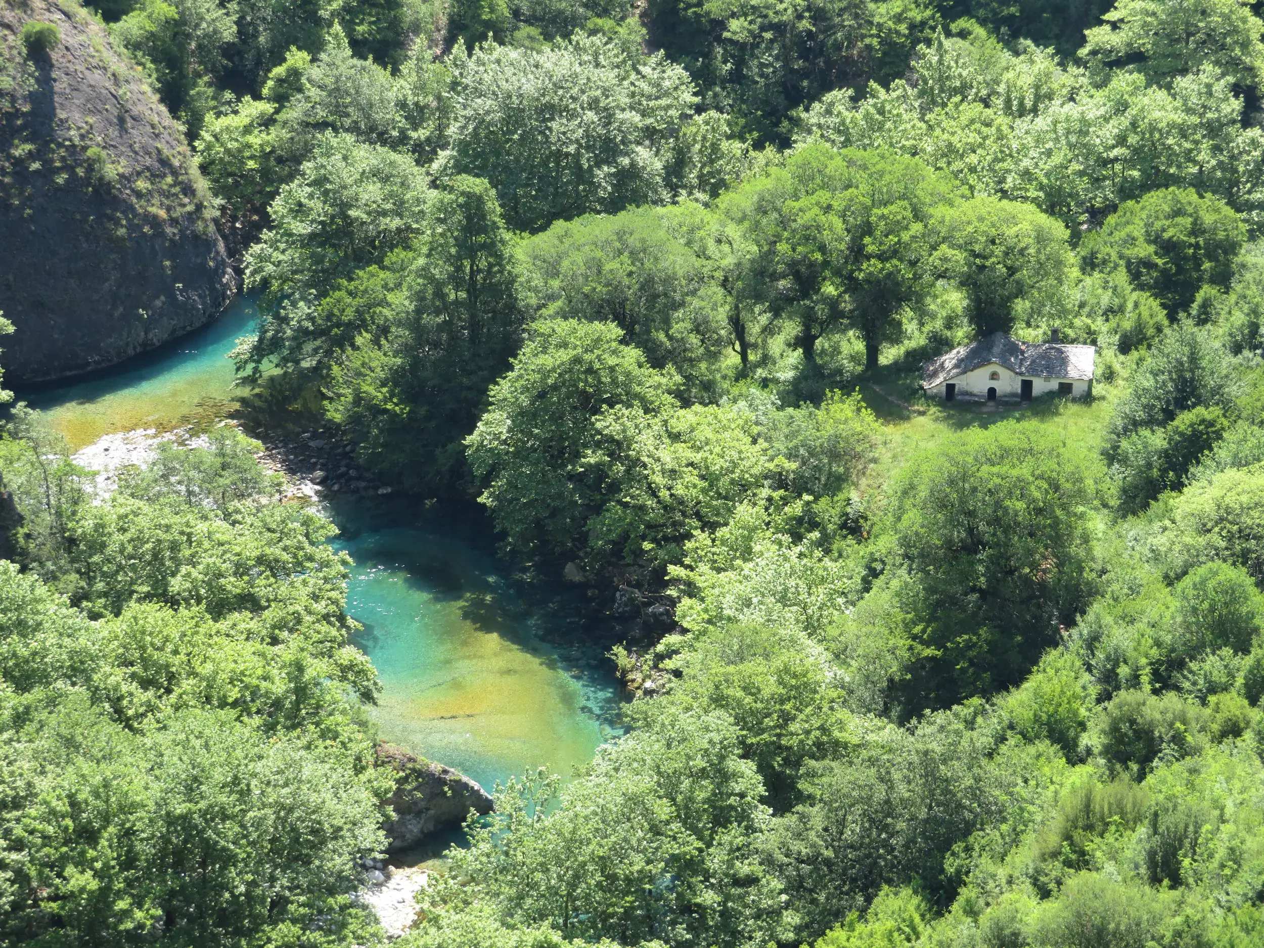 Blick von oben auf den türkisfarbenen Voidomatis-Fluss und eine kleine Kapelle in der grünen Zagori-Region.