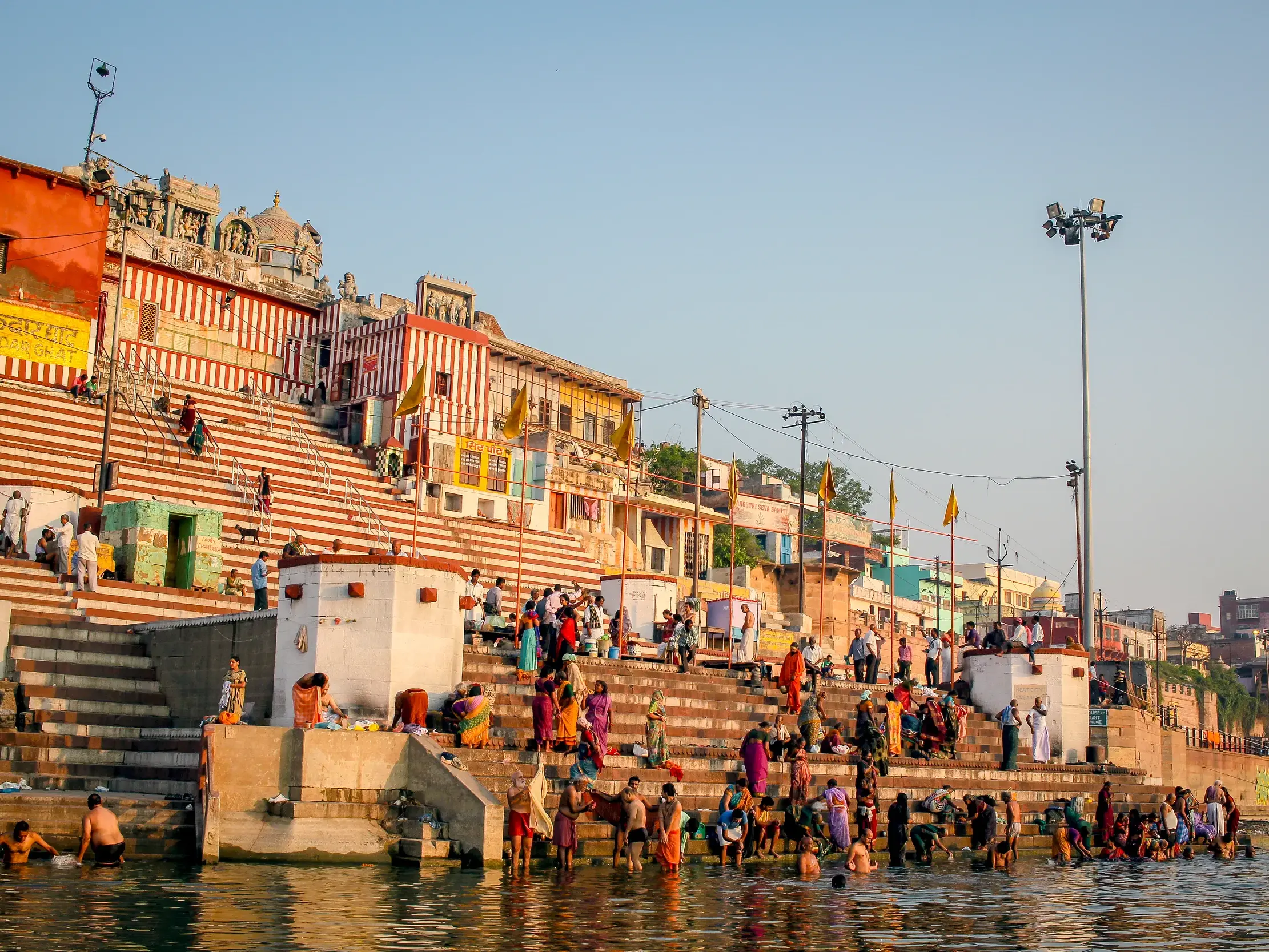 Pilger bei einem rituellen Bad im heiligen Fluss Ganges an den bunten, stufenartigen Ghats von Varanasi bei Sonnenaufgang.