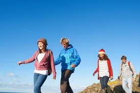 Vier gut gelaunte junge Leute wandern auf einer Gruppenreise über einen felsigen Pfad in der Mongolei bei strahlend blauem Himmel.