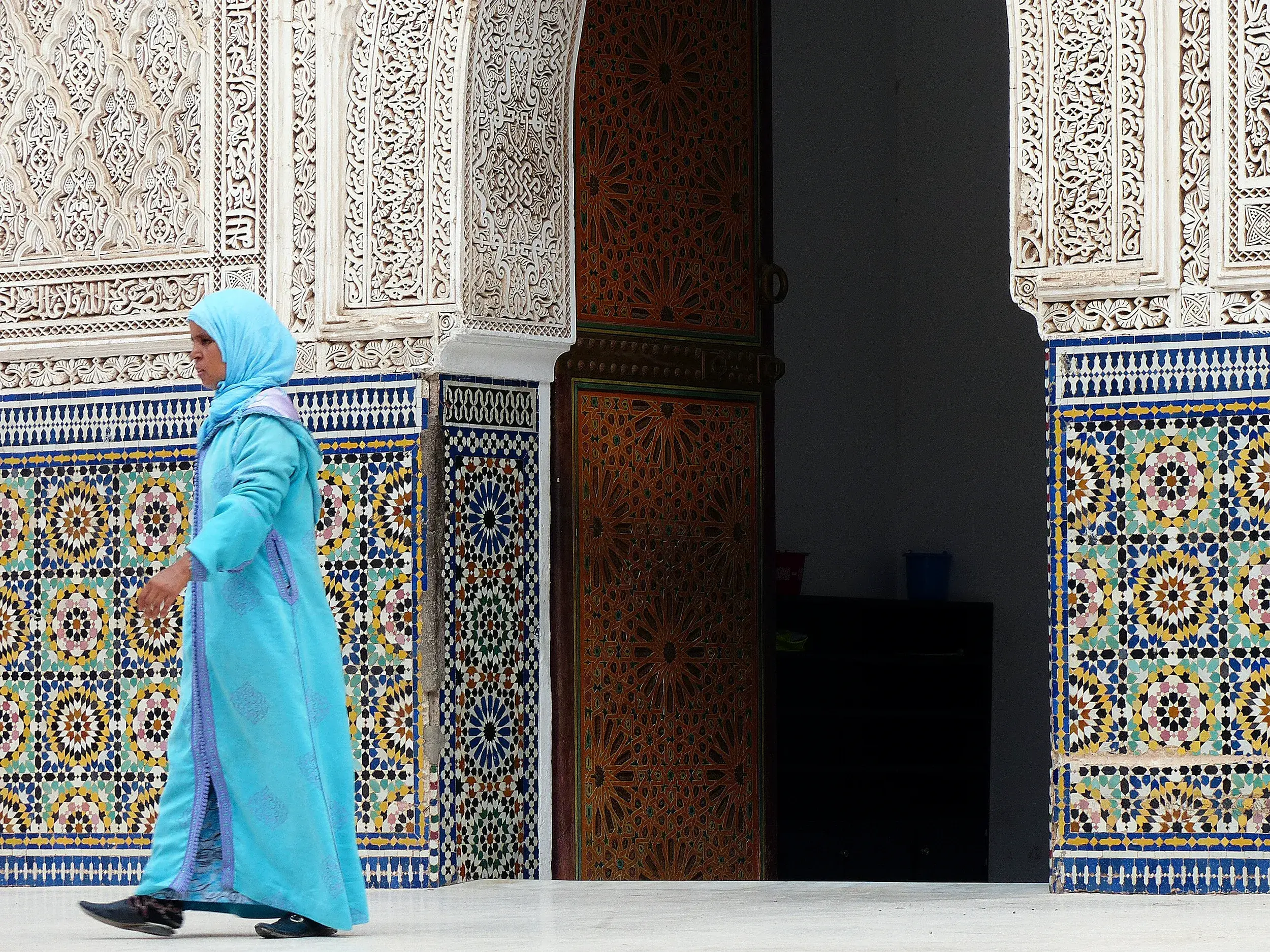 Einheimische Frau in traditioneller Kleidung vor den kunstvollen Mosaiken und Stuckarbeiten in der Medina von Marrakesch.