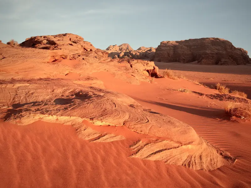 Goldene Abendsonne beleuchtet die roten Sanddünen und bizarren Felsformationen in der Wüstenlandschaft des Wadi Ram, Jordanien.