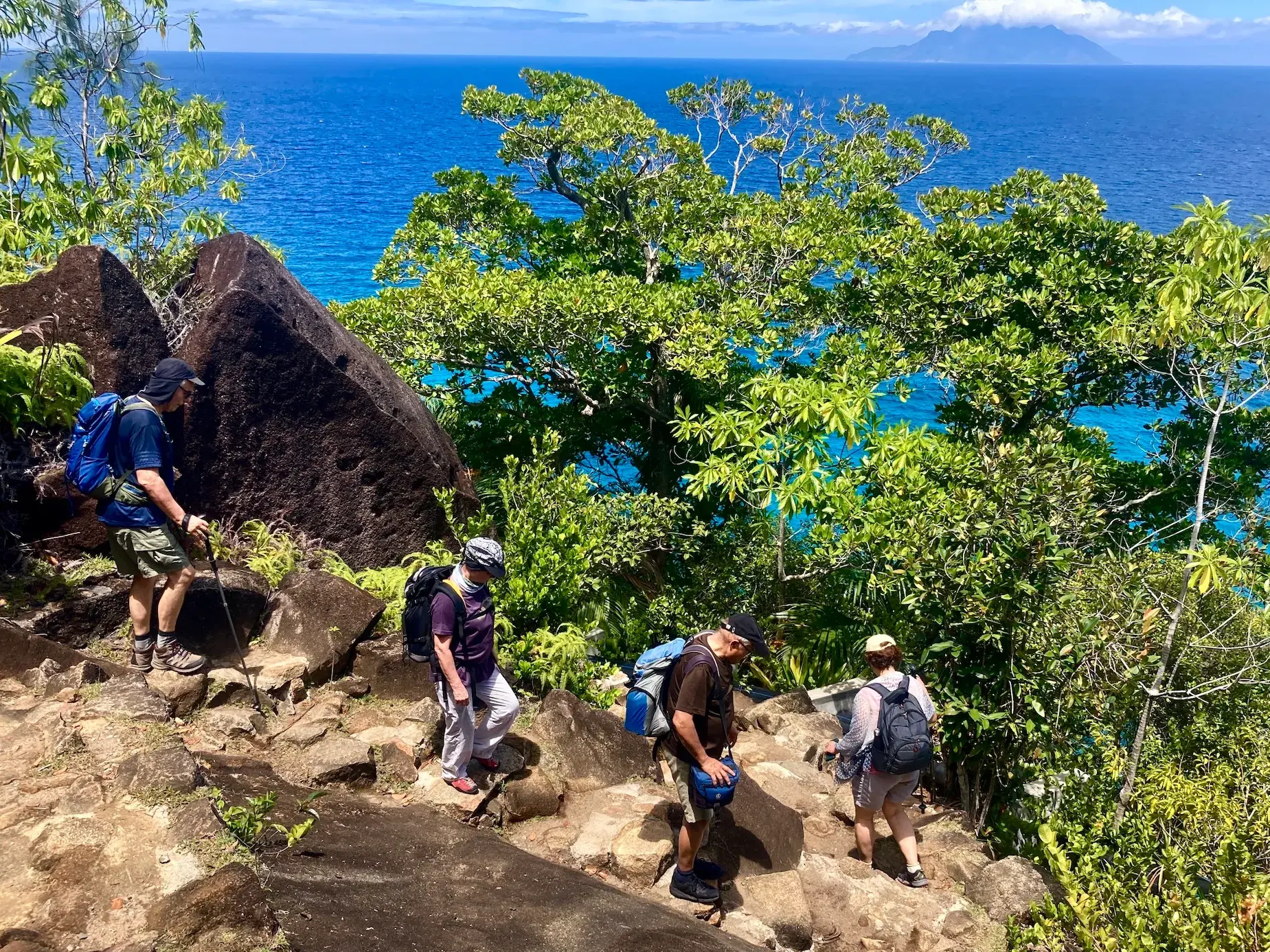 Eine Reisegruppe beim Wandern über einen felsigen Küstenpfad auf den Seychellen mit Blick auf den Indischen Ozean.