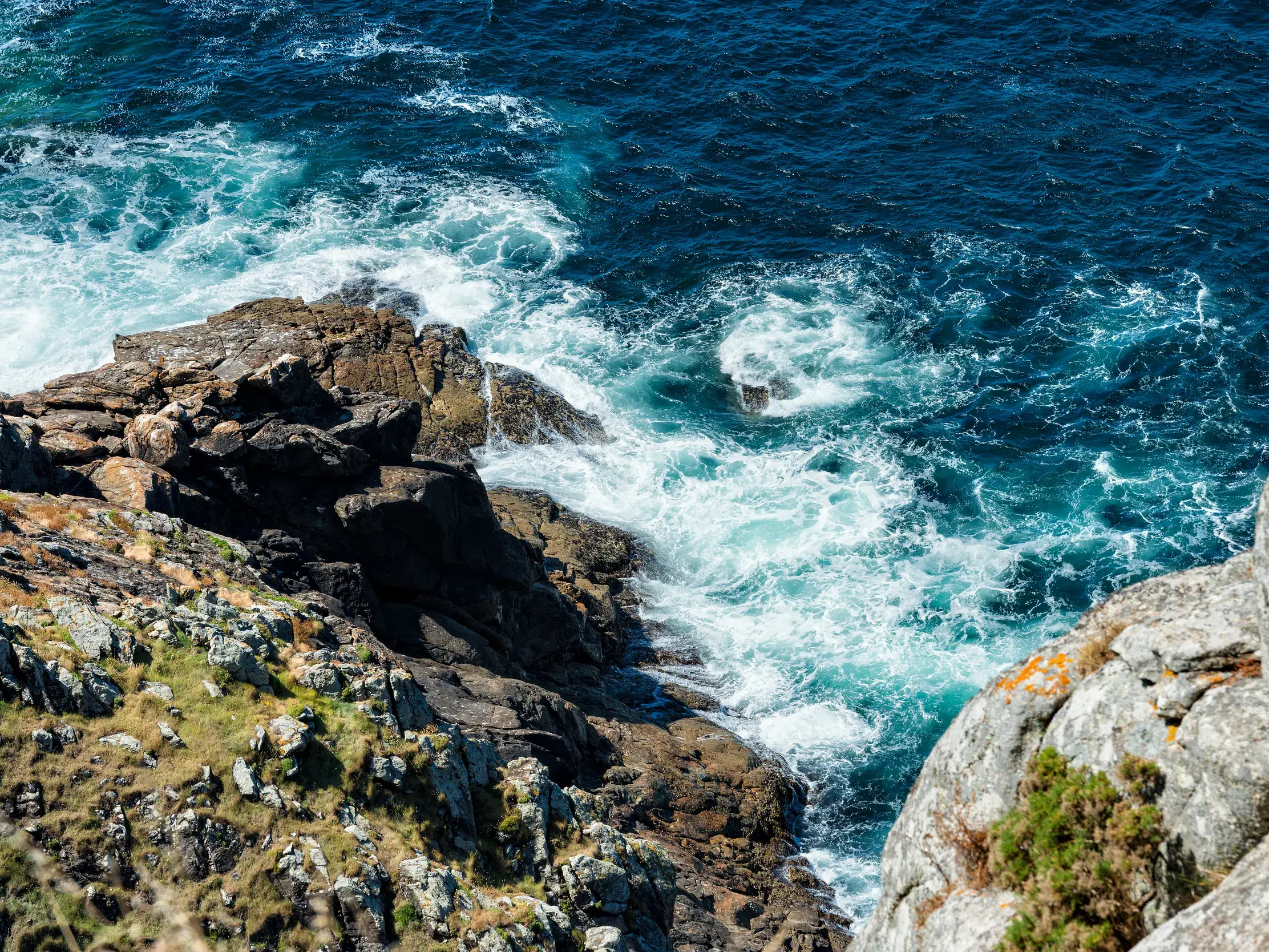 Blick von oben auf die wilde, felsige Atlantikküste Galiciens, wo die blaue Brandung tosend an die Klippen schlägt.