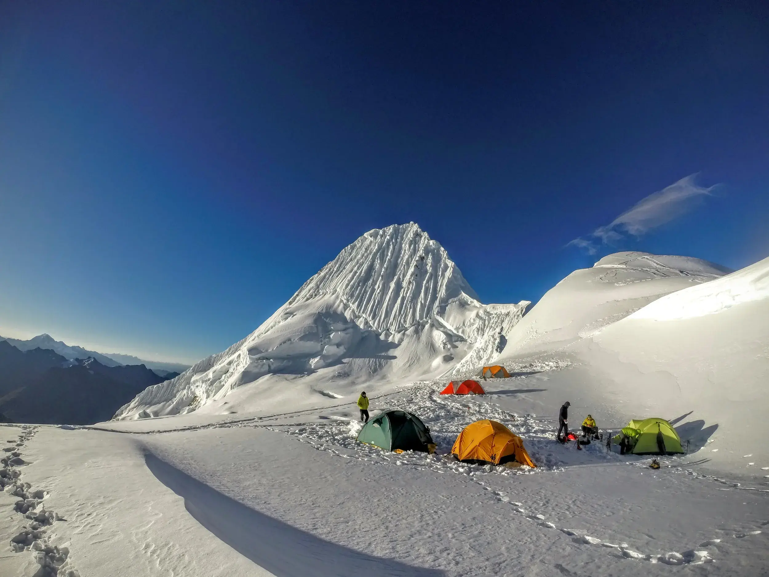Bunte Expeditionszelte im Alpamayo-Hochlager vor der beeindruckenden Eiswand des Gipfels in der Cordillera Blanca.