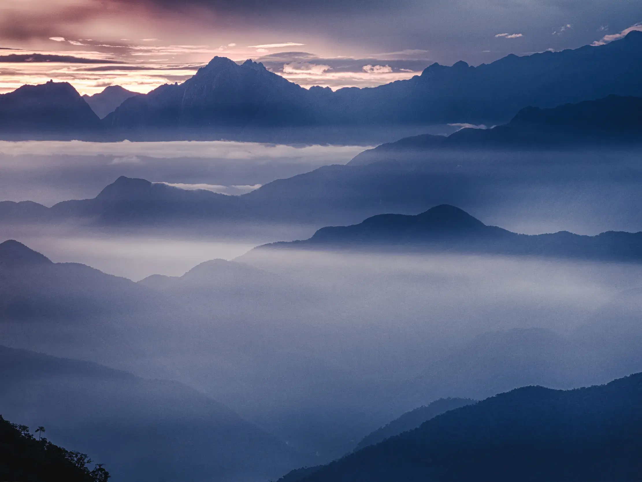 Gestaffelte Bergsilhouetten im Los Nevados-Nationalpark in Kolumbien ragen bei Sonnenaufgang aus einem dichten Nebelmeer empor.