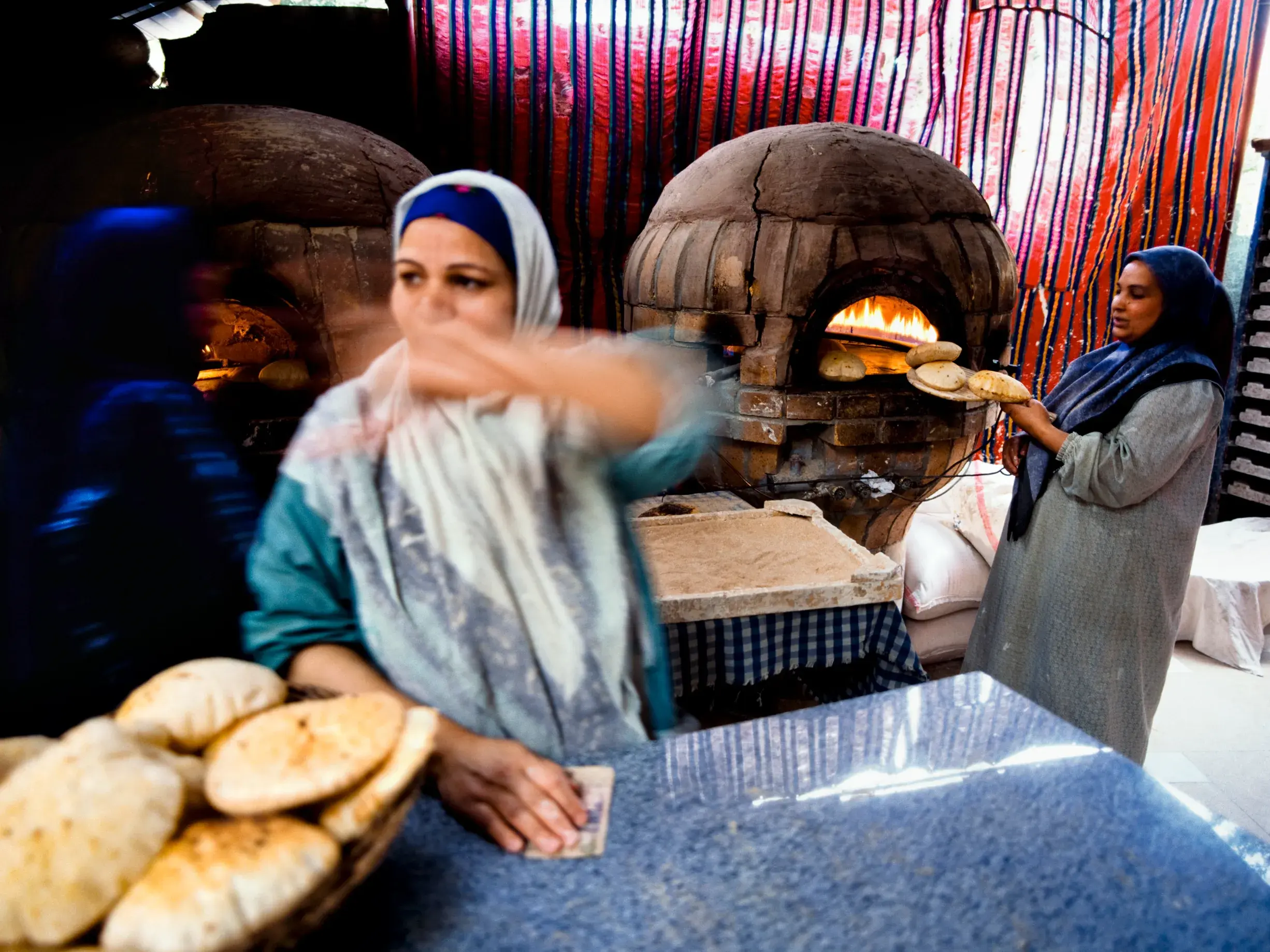 Authentische Szene in einer Bäckerei in Kairo: Zwei Frauen backen traditionelles Fladenbrot in kuppelförmigen Lehmöfen.