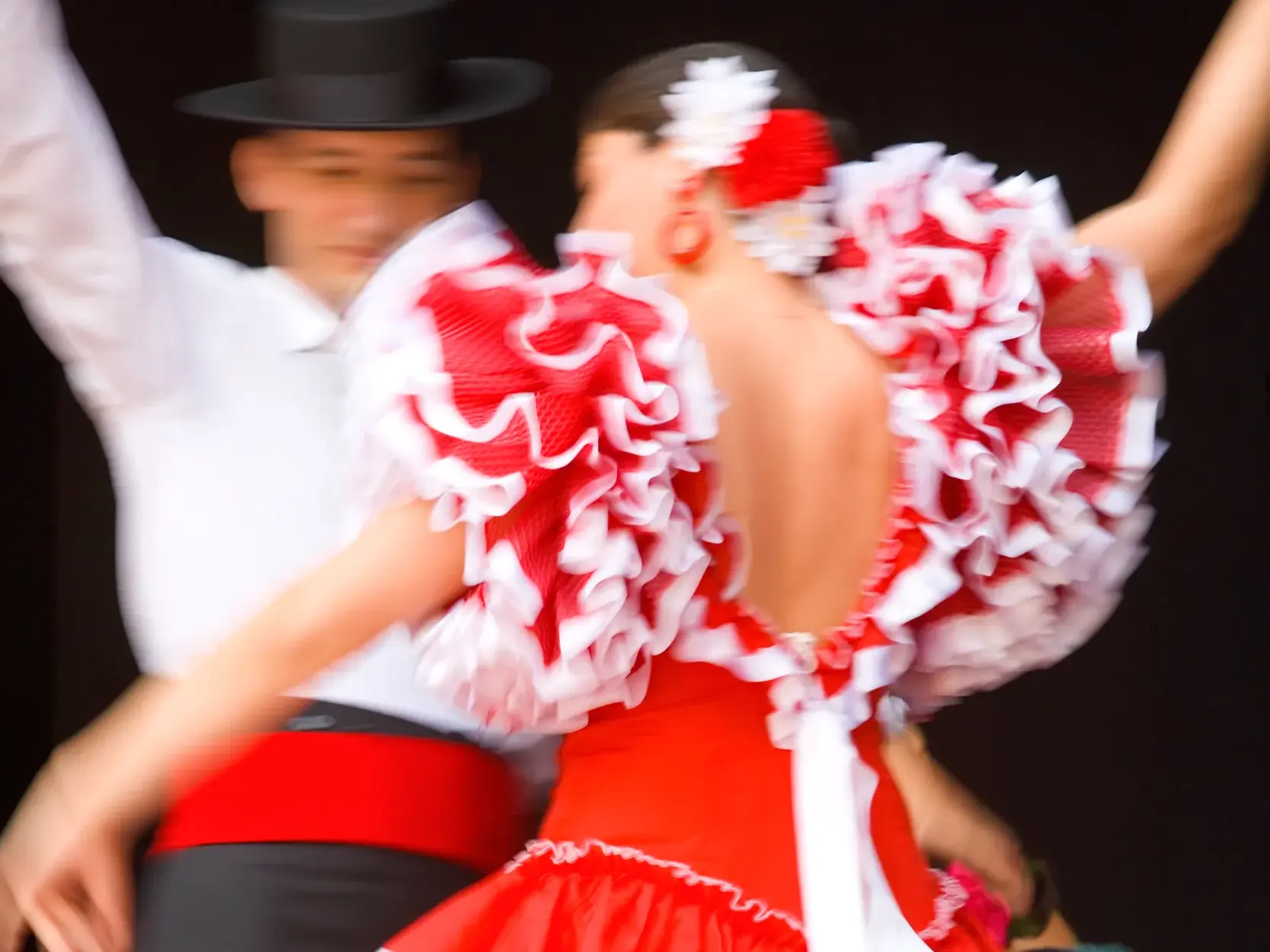 Authentischer Flamenco-Tanz: Nahaufnahme eines Paares in Bewegung, das rote Rüschenkleid der Tänzerin wirbelt dynamisch.