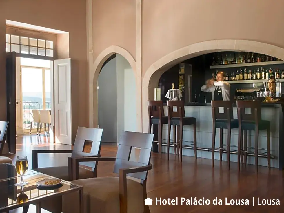Elegante Lounge-Bar im Hotel Palacio Lousa in Lousa mit Holzboden und einem Barkeeper, der einen Cocktail mixt.