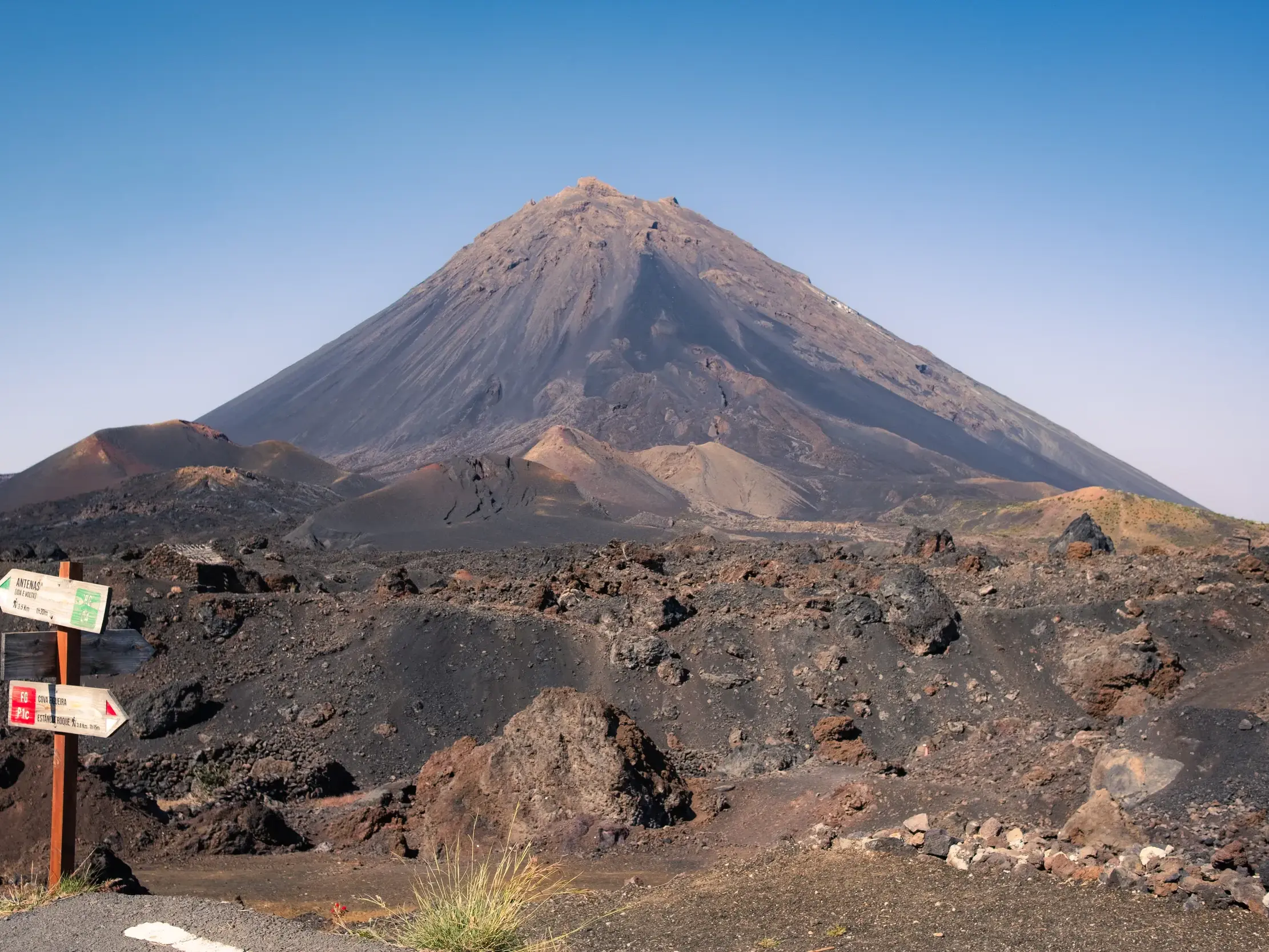 Wegweiser für Wanderer in der kargen Vulkanlandschaft der Chã das Caldeiras mit Blick auf den Gipfel des Pico do Fogo.