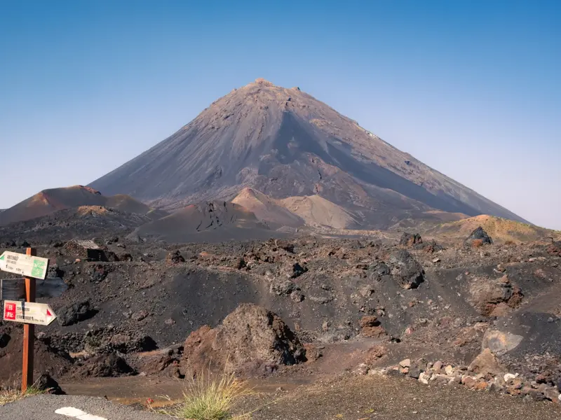 Wegweiser für Wanderer in der kargen Vulkanlandschaft der Chã das Caldeiras mit Blick auf den Gipfel des Pico do Fogo.