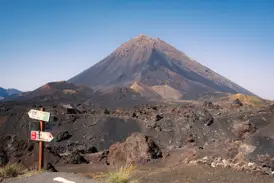 Wegweiser für Wanderer in der kargen Vulkanlandschaft der Chã das Caldeiras mit Blick auf den Gipfel des Pico do Fogo.