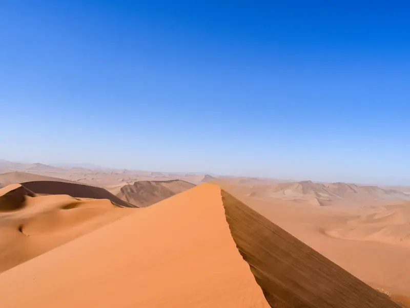 Schmaler Grat einer leuchtend roten Sanddüne bei Sossusvlei, mit Weitblick über das endlose Dünenmeer der Namib-Wüste.