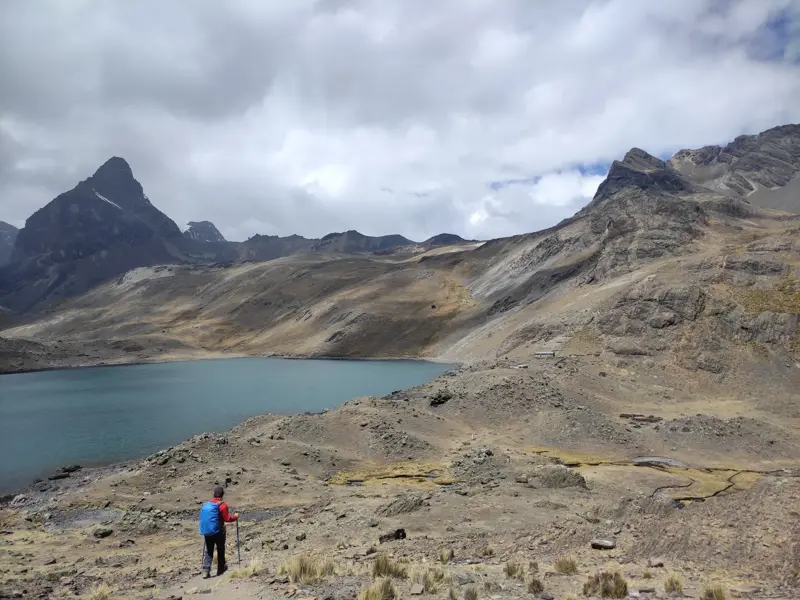 Ein Wanderer mit Trekkingstöcken und Rucksack auf einem Pfad oberhalb der Laguna Chiar Khota im Condoriri Gebirge Boliviens.
