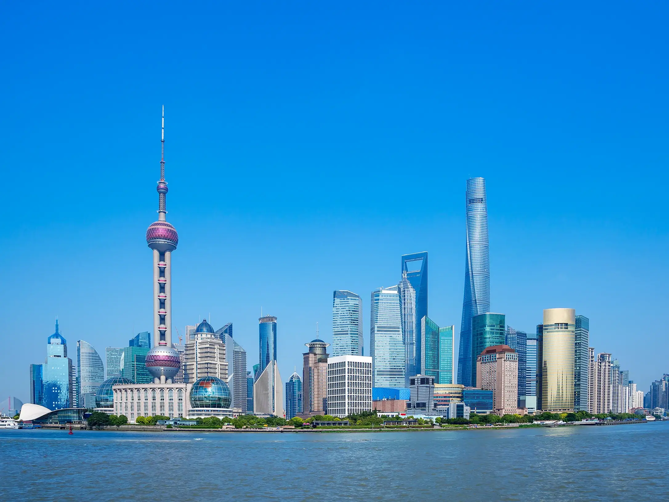 Blick von der Uferpromenade Bund auf die moderne Skyline von Shanghai mit dem Oriental Pearl Tower und Wolkenkratzern bei klarem Himmel.