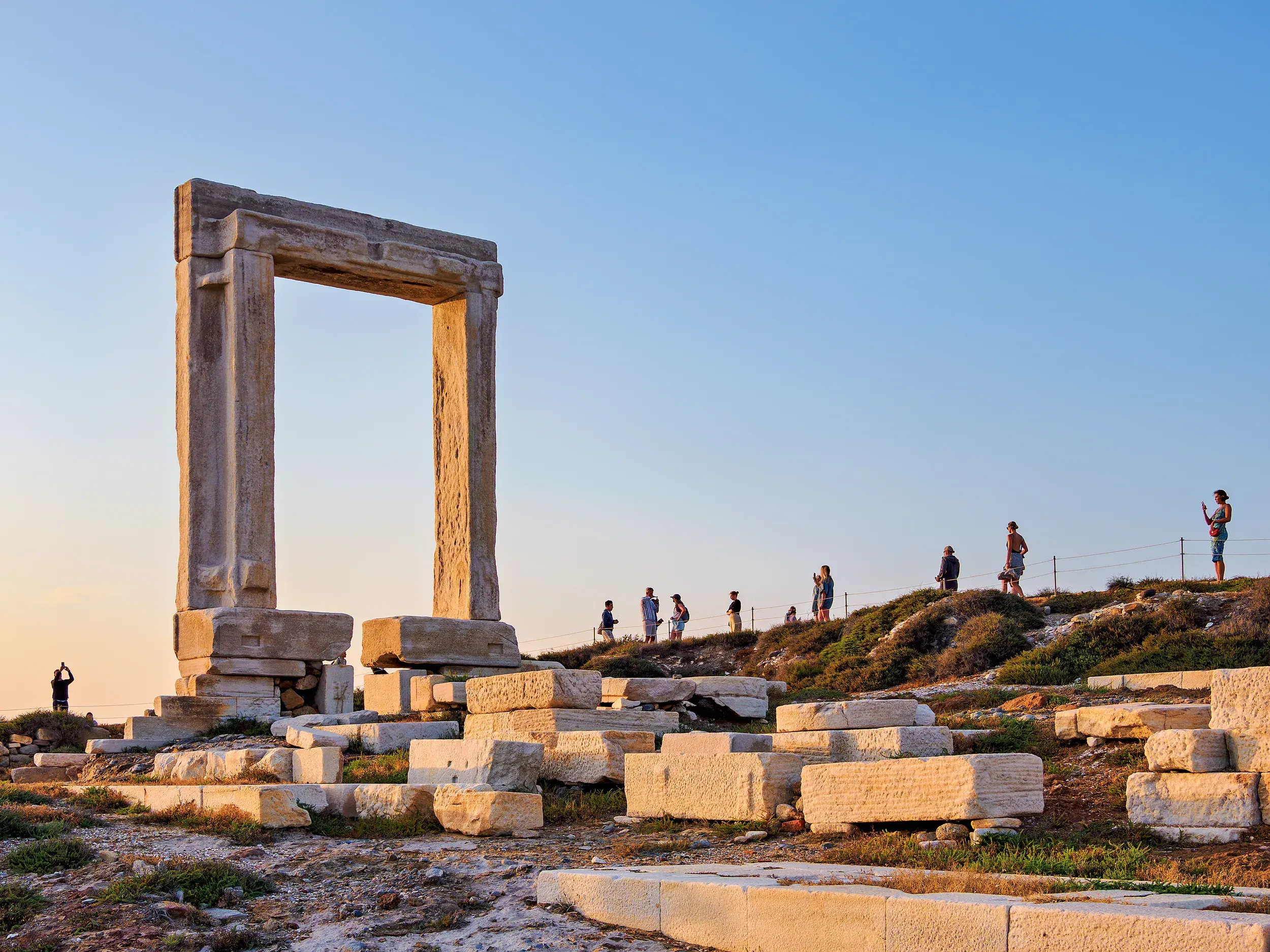 Eine Gruppe junger Leute einer Rundreise genießt den Sonnenuntergang am antiken Marmortor Portara auf der Insel Naxos.