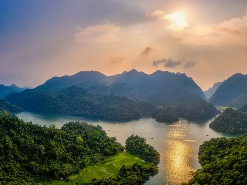 Goldener Sonnenuntergang über dem Ba Be See im Nationalpark in Vietnam, umgeben von grünen Karstbergen und Reisterrassen.